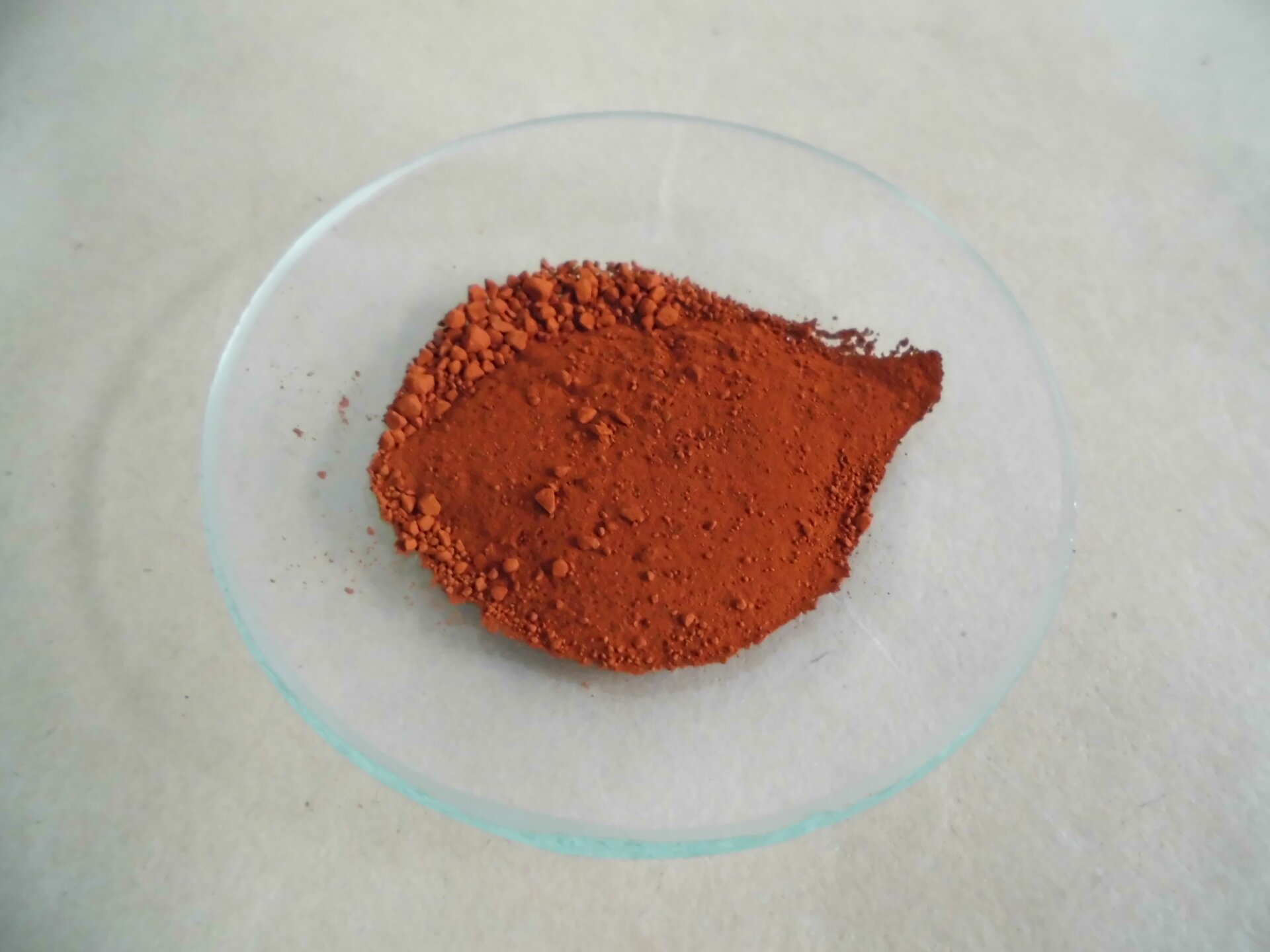 Na zdjęciu na szkiełku zegarkowym jest pomarańczowy proszek. 