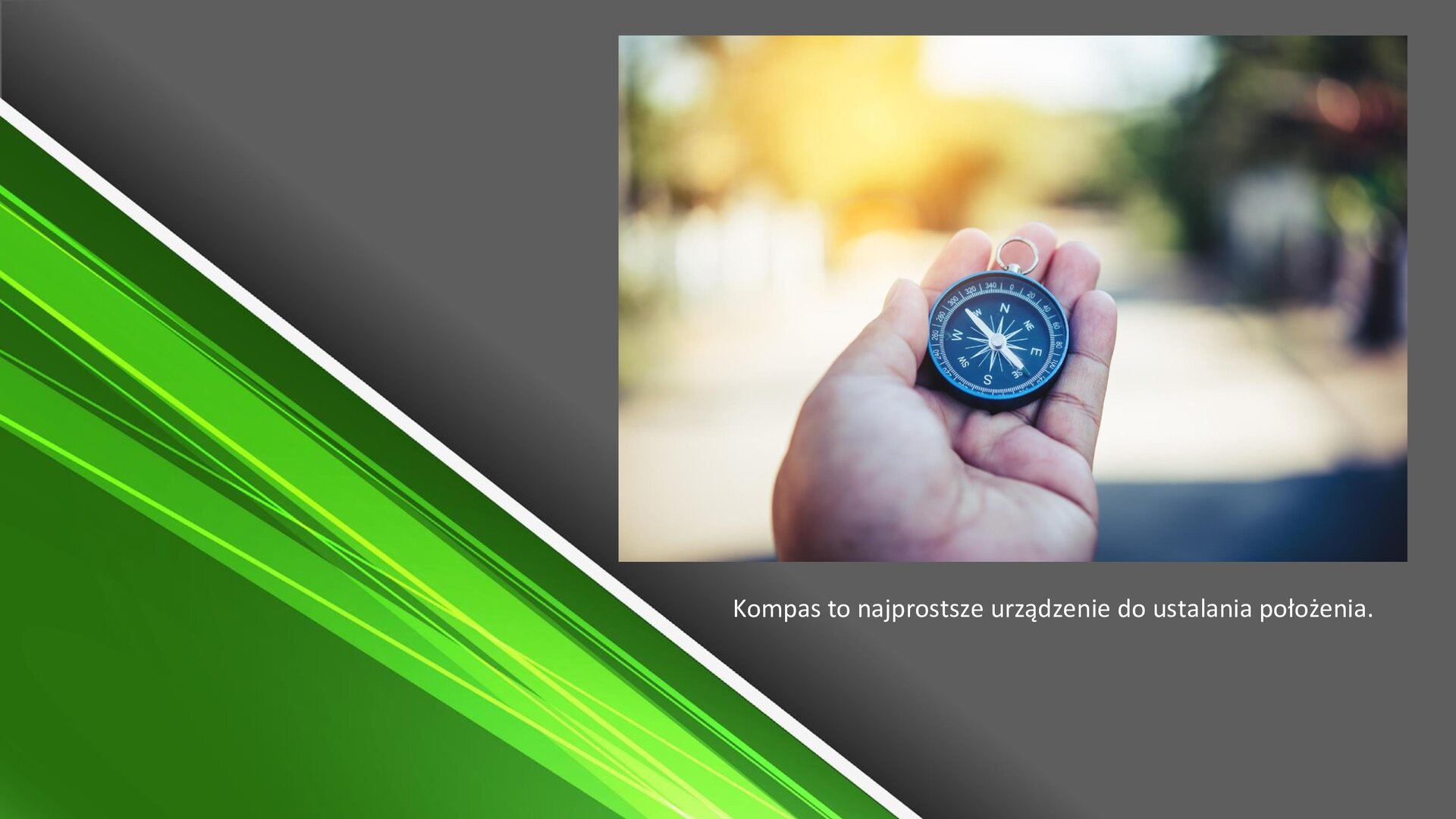 Zielono‑szary slajd. W prawym górnym rogu zdjęcie przedstawiające dłoń, na której leży czarny kompas. Pod zdjęciem tekst: „Kompas to najprostsze urządzenie do ustalania położenia”.