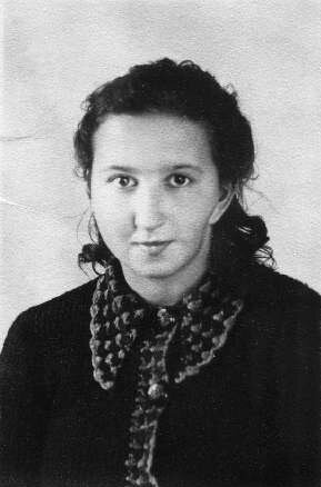 Zdjęcie przedstawia młodą kobietę. Ma półdługie, ciemne włosy, luźno spięte na karku, okrągłą twarz, wysokie czoło, wyraziste oczy, wąskie brwi, kształtny nos i usta. Ubrana jest w ciemną, jednolitą bluzkę na guziki. Dłuższe kołnierzyki bluzki i plisa wzdłuż guzików są wzorzyste.