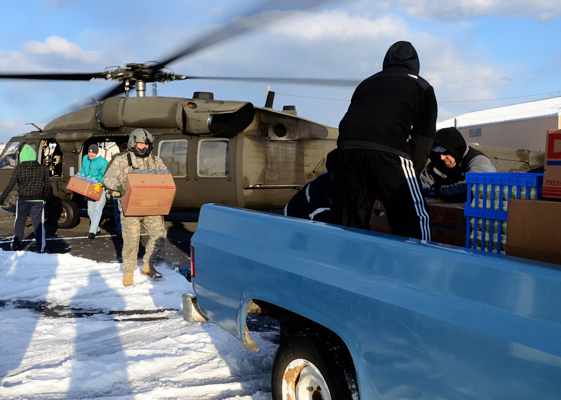 Żołnierz i cywile przenoszą kartony z żywnością ze śmigłowca na półciężarówkę.