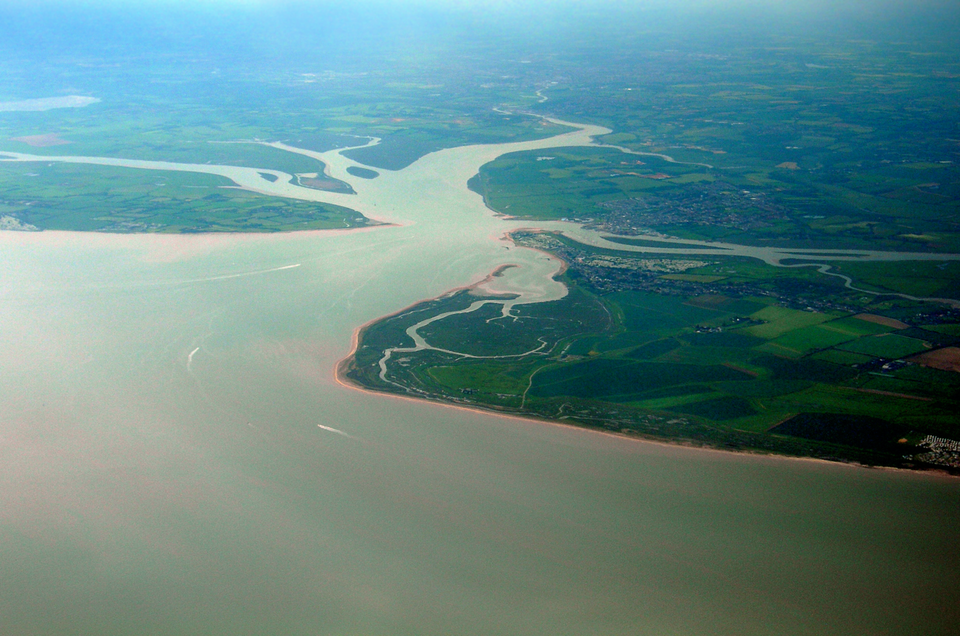 Na zdjęciu lotniczym ujście lejkowate rzeki Colne w Wielkiej Brytanii. Na pierwszym planie bardzo szerokie ujście rzeki, w tle stopniowo zwężający się dolny bieg. Brzegi rzeki płaskie, porośnięte zieloną roślinnością.