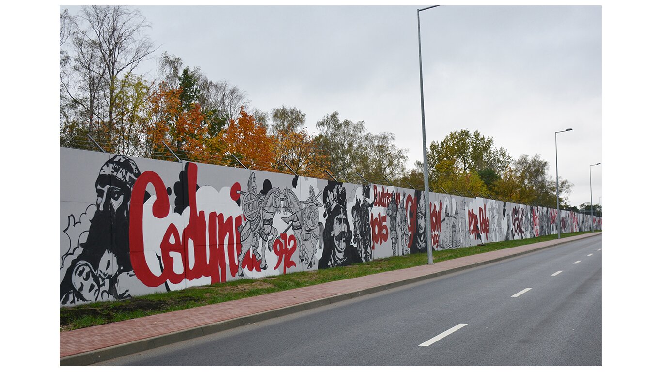 Fotografia barwna przedstawiająca mural patriotyczny. Mural w Legionowie przedstawia 1050 lat chwały i męstwa polskiego oręża. Mural ma aż 750 metrów długości. Na pierwszym planie portret Mieszka I i bitwa pod Cedynią w 972 roku.