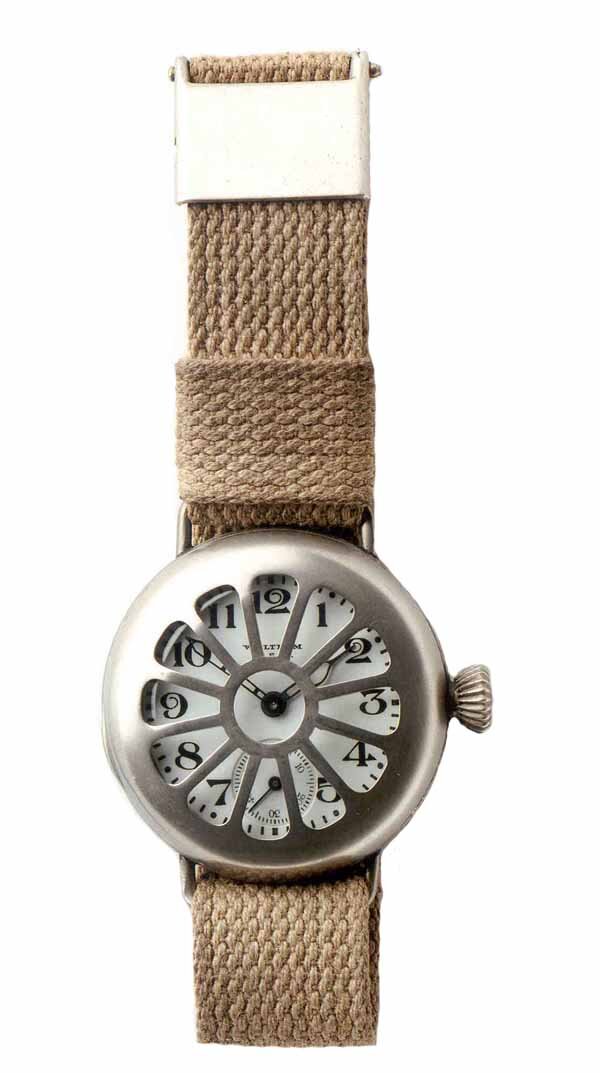 Zdjęcie przedstawia zegarek ze wskazówkami ustawionymi na godzinie pierwszej i pięćdziesiąt minut. Jego tarcza jest biała z czarnymi cyframi. Posiada ażurową osłonę z metalu. Pasek zegarka jest zrobiony z brązowego materiału.