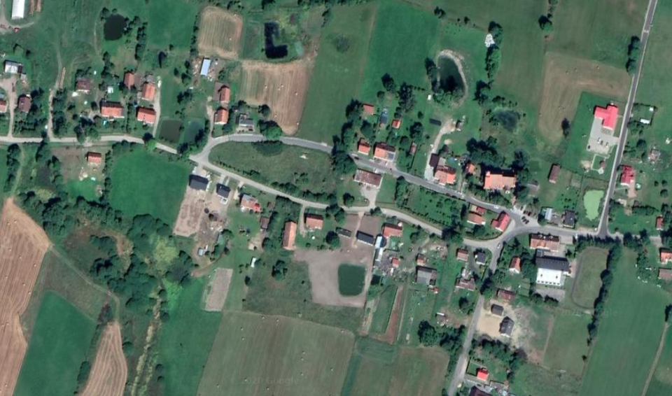 Zdjęcie przedstawia widok z góry na ulicę, tworząca owal. Wokół owalu są zabudowania. Teren jest płaski, widać na nim liczne pola. 