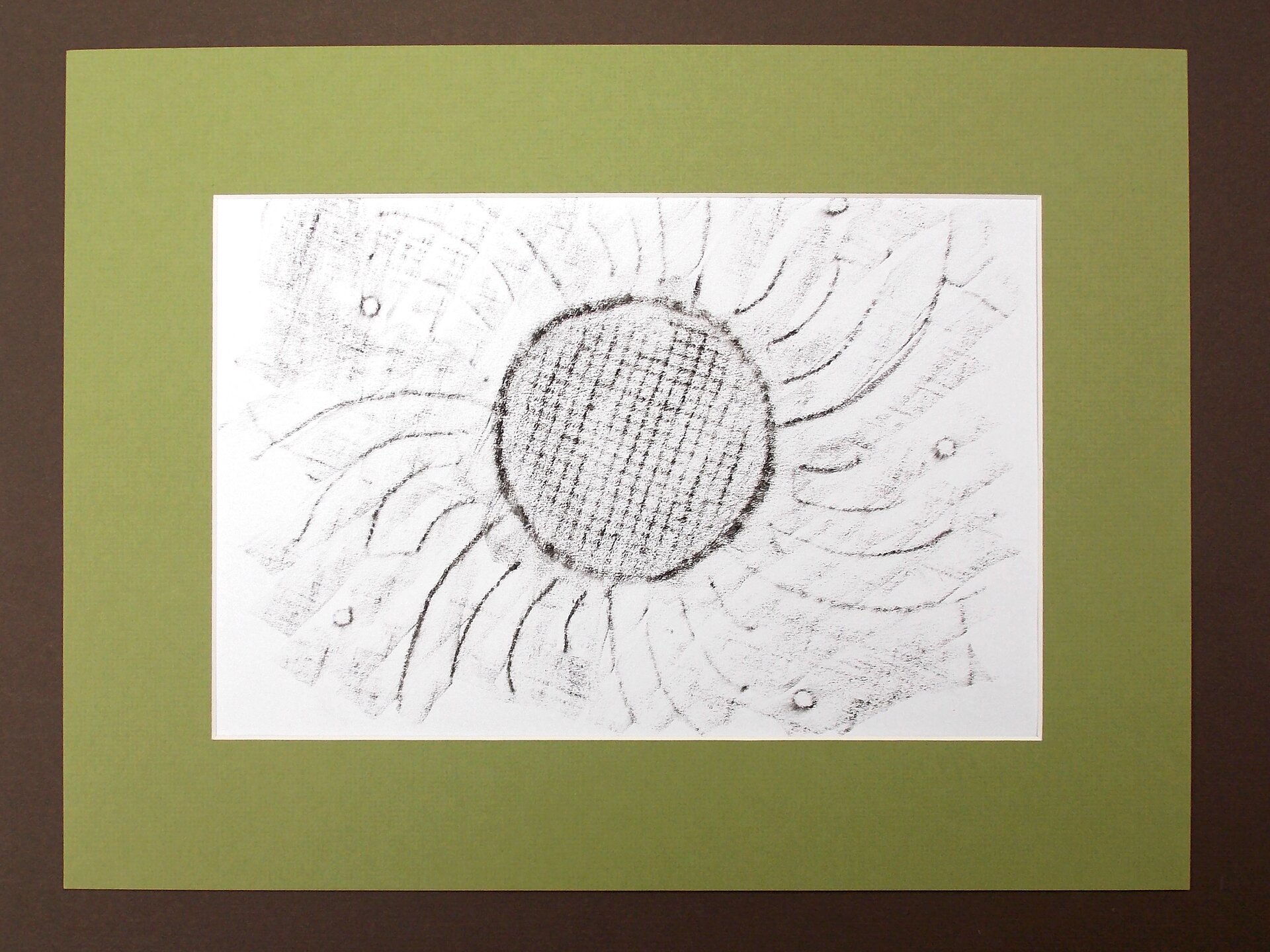 Ilustracja przedstawia grafikę wykonaną w technice frotażu. Jest to odbitka wzoru serwetki. Czarno‑biała praca ukazuje kwiat o dużym okrągłym środku z wnętrzem pokrytym kratkowym deseniem. Na około środka znajdują się linie płatków oraz widoczne gdzieniegdzie małe, okrągłe kółeczka. Na grafice można również rozpoznać odbity wzór powierzchni tkaniny. Praca oprawiona jest w podwójne  passe‑partout  [czytaj: pas partu] składające się z dwóch papierowych ramek. Brązowa, węższa znajduje się na zewnątrz, natomiast szersza, zielona, wewnątrz okala obrazek.