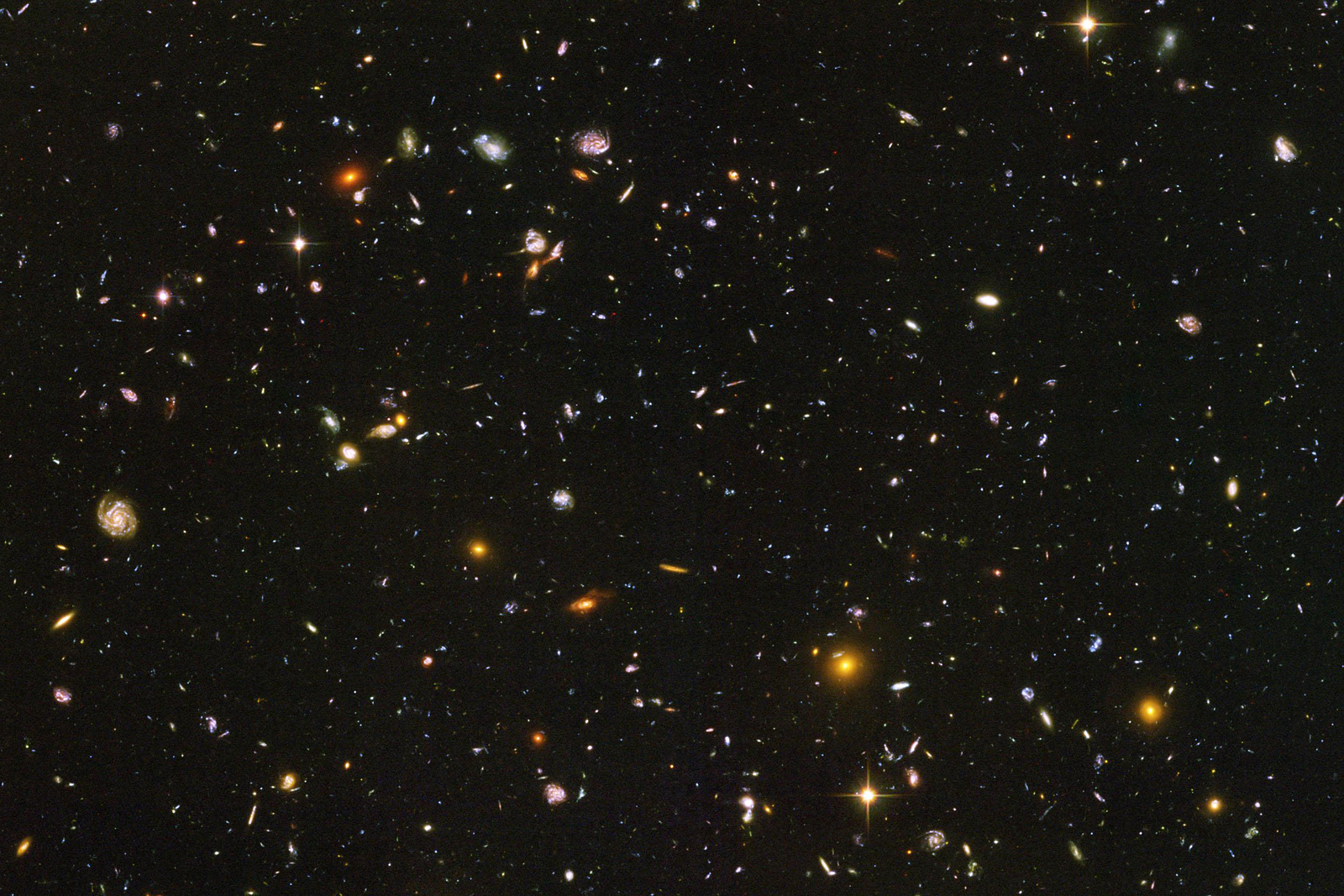 Fotografia wykonana z teleskopu umieszczonego w kosmosie. Na czarnym tle widoczne są liczne mniejsze i większe punkty. Są to galaktyki.