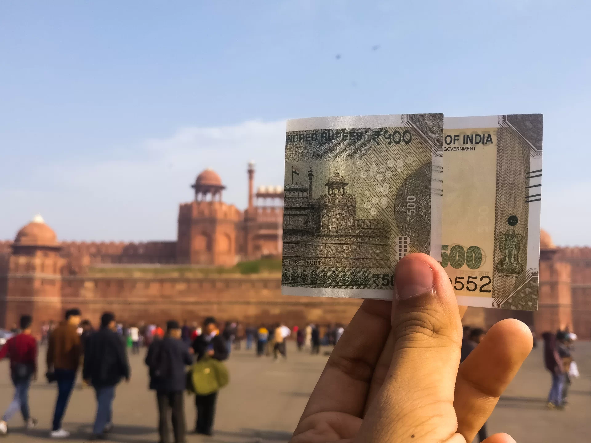 Fotografia przedstawiająca wymuszoną perspektywę dopasowującą ilustrację na banknocie do Czerwonego Fortu w Delhi. Osoba trzymająca w palcach banknot indyjski przykłada go do panoramy na Czerwony Fort z odpowiedniej odległości, w odpowiednim miejscu, tak aby rzeczywisty krajobraz naturalnie przechodził w ilustrację na banknocie.  