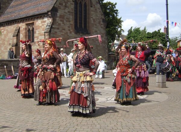 Zdjęcie, które przedstawia taniec, który jest prezentowany przez Romki na dziedzińcu zamkowym. Stroje tańczących Romek charakteryzują się jasnymi, nasyconymi barwami oraz swego rodzaju pstrokacizną. Na głowie każdej nich jest nakrycie, które tworzy rodzaj turbanu.