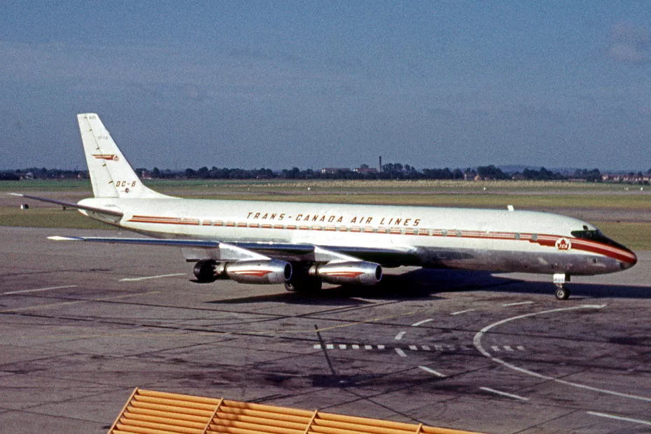 Kliknij, aby powiększyć Zdjęcie. Na płycie lotniskowej stoi samolot. Jest ustawiony dziobem w prawą stronę. Jest koloru białego z napisami Trans- Canada Air Lines.