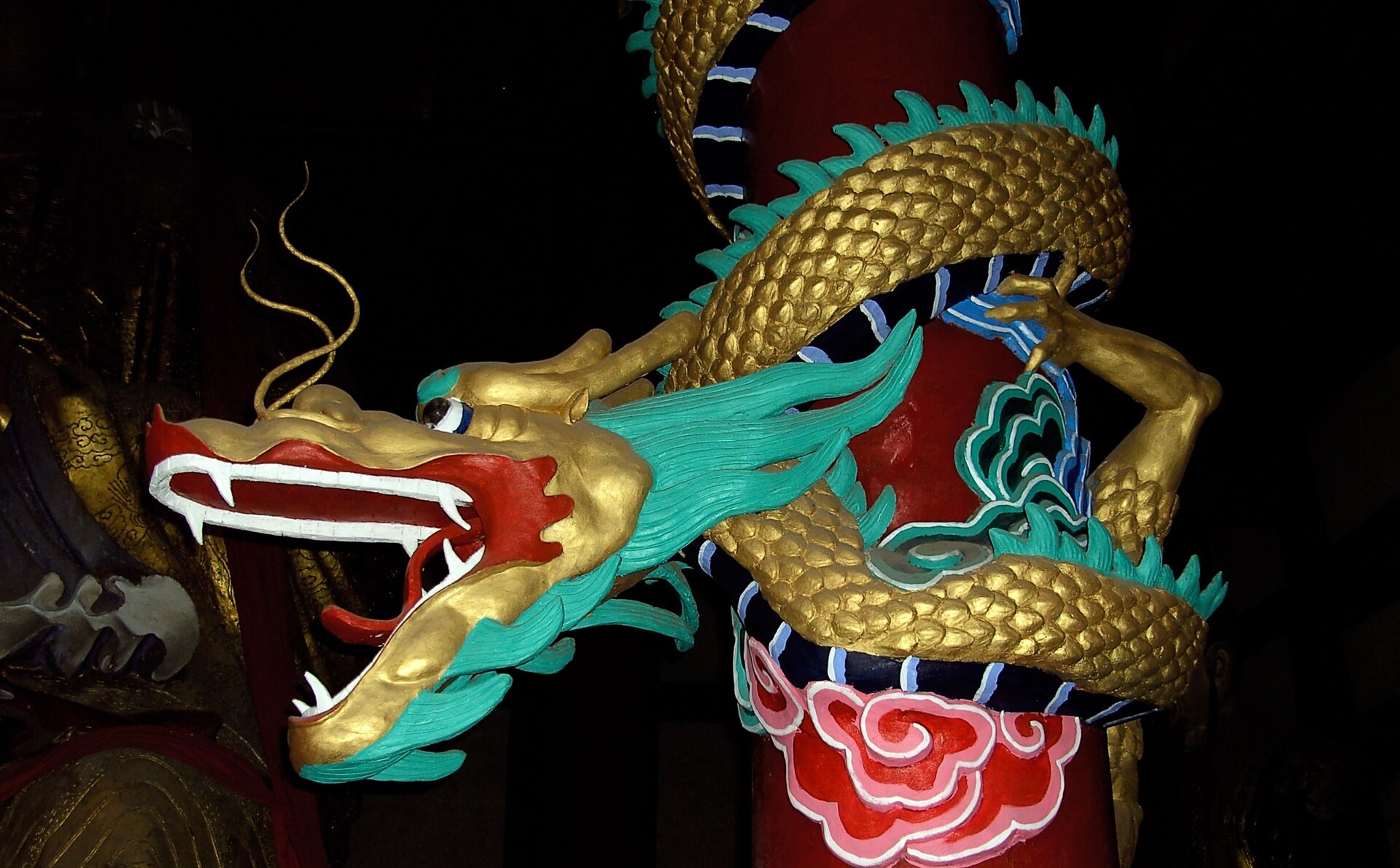 Kliknij, aby powiększyć. Na zdjęciu smok w starożytnym mieście duchów Fengdu w Chinach. Rzeźba smoka, który owija się wokół czerwonego słupa. Smok przypomina węża, jest złoto‑zielony, ma otwarta paszcze i długie wąsy.