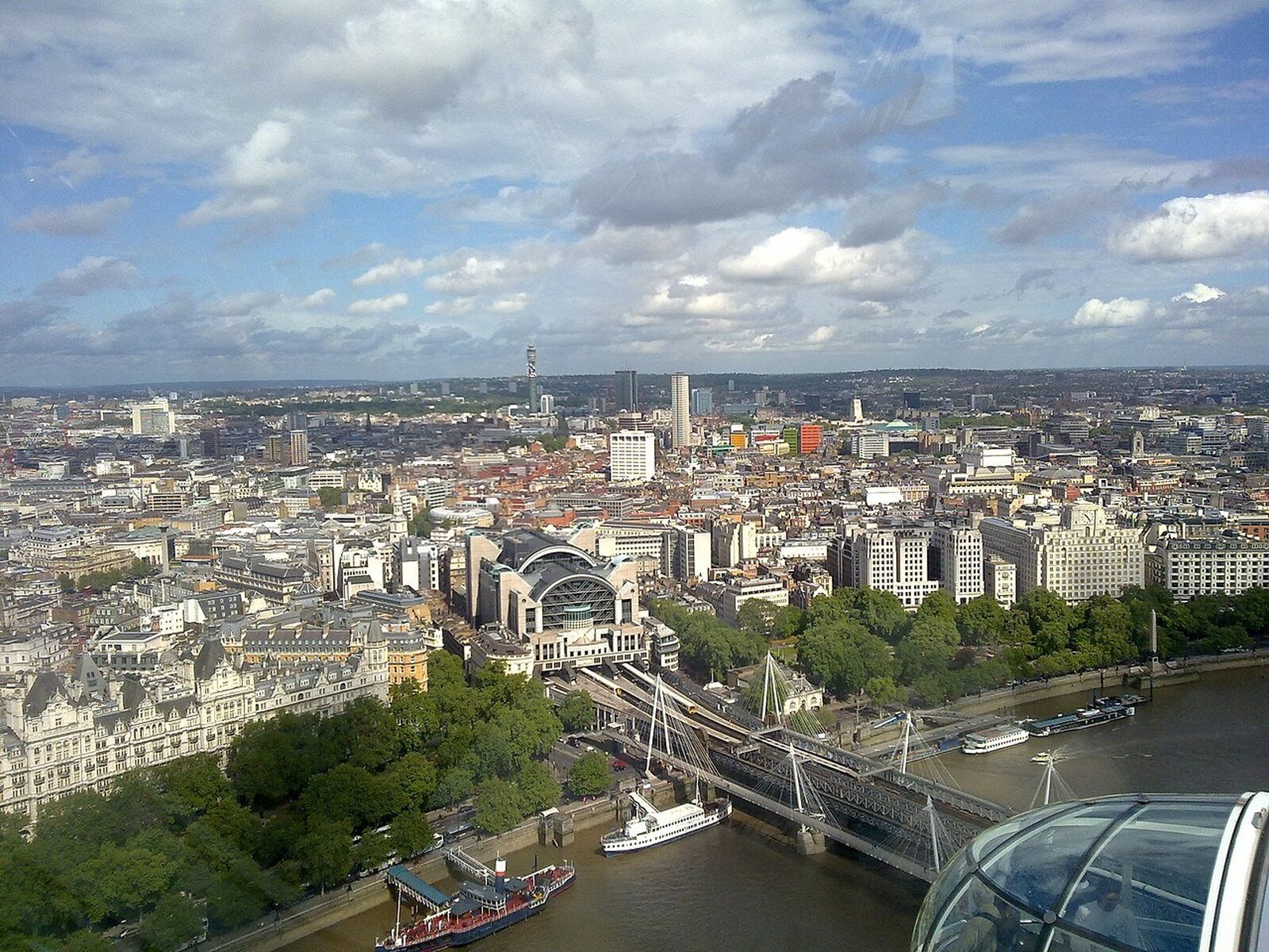Fotografia lotnicza jednej z dzielnic Londynu. Na pierwszym planie rzeka, most, dalej gęsta miejska zabudowa złożona z kamienic, na drugim planie wieżowce.