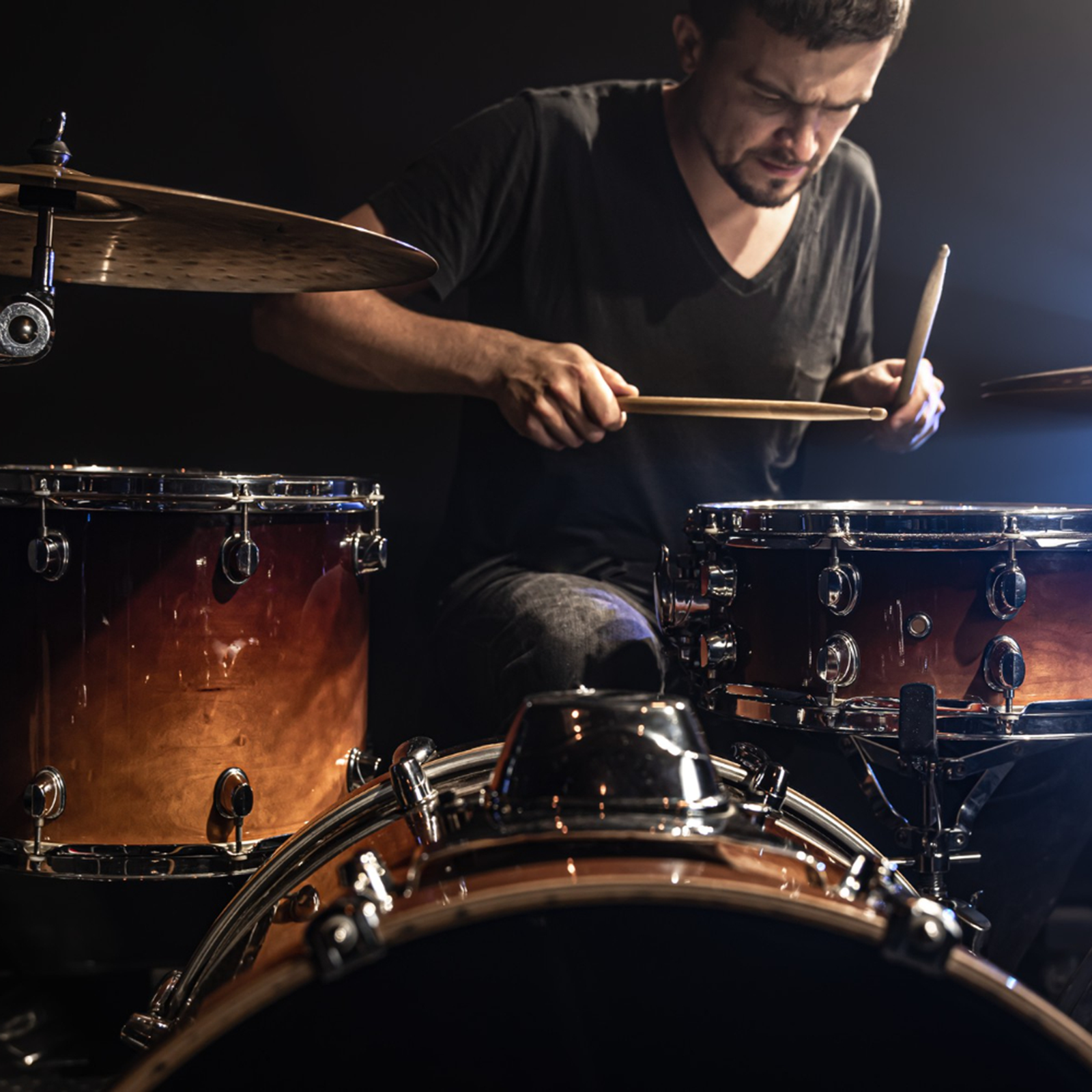 Ilustracja przedstawia mężczyznę, siedzącego przy perkusji. Mężczyzna uderza pałeczkami w werble.