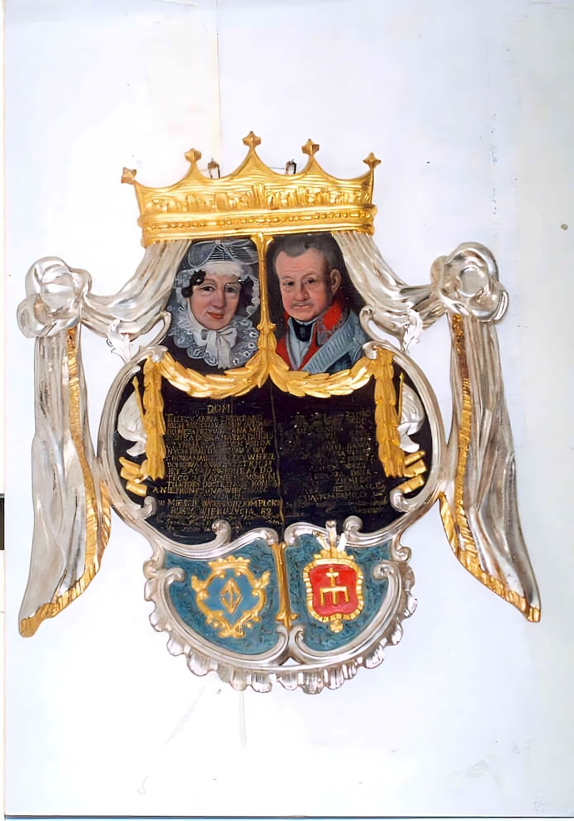 Ilustracja przedstawia dwie czarne tablice z wyrytymi na nich nieczytelnymi napisami. Tablice są otoczone złotym ozdobnym łańcuchem przypominającym udrapowane na kształt kurtyny liście. Nad lewą tablicą znajduje się portret starszej kobiety w białym czepku i z białą kokardą pod brodą. Kobieta ma też rozłożysty biały kołnierz. Widać jej lekko uśmiechniętą twarz i kilka pukli czarnych, kręconych włosów. Nad prawą tablicą znajduje się portret starszego mężczyzny z siwymi, zaczesanymi do tyłu włosami. Mężczyzna ma na sobie czerwony strój z wysokim kołnierzem, spod którego wystają szaro‑czarne elementy. Na lewym ramieniu ma również fragment szarego materiału. Nad portretami znajduje się duża złota korona, spod której zwisają dwie białe szarfy ze złotymi obszyciami. Są one udrapowane na kształt kurtyny. Pod tablicami znajdują się dwa herby na błękitnym tle. Z lewej strony widać błękitną tarczę ze złotym obramowaniem, wewnątrz której znajduje się złoty element w kształcie rombu. Z prawej strony widać czerwoną tarczę ze złotym obramowaniem, wewnątrz której znajduje się złoty trójząb skierowany zębami w dół oraz złoty krzyż umieszczony nad nim.