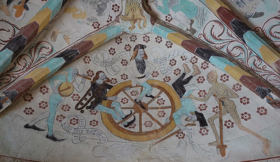 Zdjęcie przedstawia sklepienie z freskiem. Na dużym kole siedzą trzej mężczyźni. Jednego z nich z koła ściąga ludzki szkielet z łopatą w dłoni. Drugiemu mężczyźnie błazen z bębenkiem na piersi i trąbką trąbi coś do ucha. Trzeci mężczyzna siedzi na kole pewnie, podpierając boki rękami. 