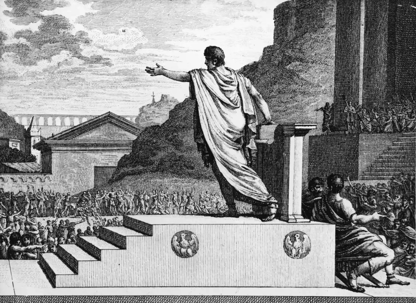 Czarno‑biała ilustracja przedstawia mężczyznę widzianego od tyłu, który stoi na podeście i występuje publicznie. Mężczyzna przemawia do tłumu, który stoi przed mównicą. 