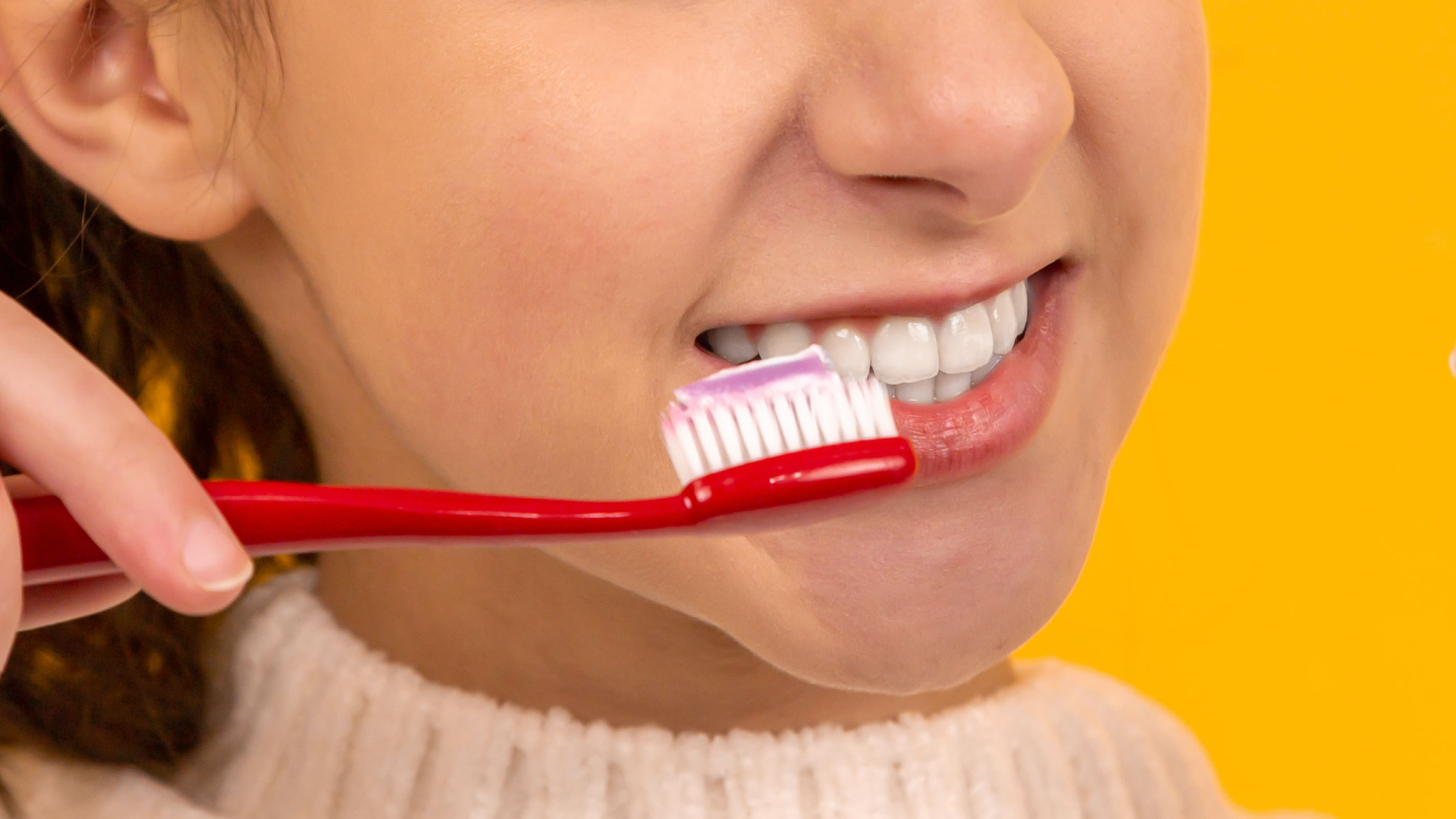 Zdjęcie przedstawia zbliżenie na usta i nos nastoletniej dziewczyny. Dziewczyna pokazuje zęby. Widać też, że dziewczyna trzyma w ręku szczoteczkę do zębów z nałożoną pastą.