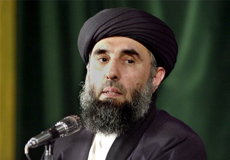 Zdjęcie przedstawia mężczyznę z długą brodą. Na głowie ma turban. Przemawia do mikrofonu.