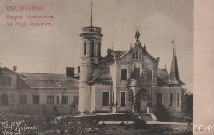 Fotografia przedstawia pałacyk. Budowla ma trzy kondygnacje. Wejście znajduje się pośrodku budynku, jest ono zadaszone. Zadaszenie jest oparte na dwóch kolumnach. Wiedzie do niego kilka schodów. Nad wejściem umieszczona jest rzeźba wyobrażająca postać w obszernej szacie. Po prawej stronie zdjęcia znajduje się czworokątny wykusz zwieńczony wieżą. W głębi, po lewej stronie stoi okrągła wieża z wąskimi oknami. Na jej umieszczony jest dość wysoki maszt.