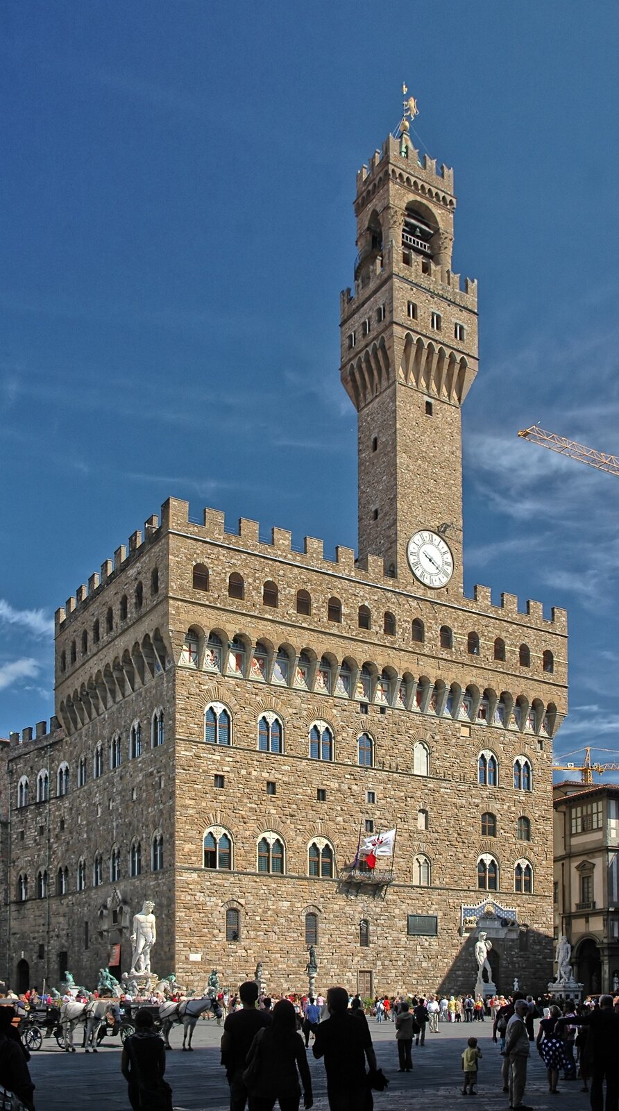 Ilustracja o kształcie pionowego prostokąta przedstawia fotografię Palazzo Vecchio we Florencji. Budowla posiada kamienne, rustykowane elewacje z dwudzielnymi oknami, zamkniętymi łukiem. Mury wieńczą blanki, pod którymi znajdują się otwory. Nad bryłą góruje wieża zegarowa, na której znajduje się dwukondygnacyjny ganek obronny z blankami. W tle znajduje się zabudowa miejska, a przed budowlą plac, po którym spacerują ludzie. 