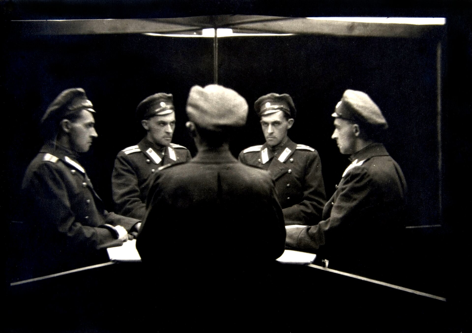 Kliknij, aby powiększyć. Fotografia ukazuje zwielokrotniony wizerunek mężczyzny ubranego w mundur. Po środku zdjęcia stoi człowiek, po jego prawej i lewej stronie widnieją lustra, w których postać się odbija. Efekt ten jest osiągnięty dzięki zastosowaniu dwóch luster. Mężczyzna stoi tyłem do widza.