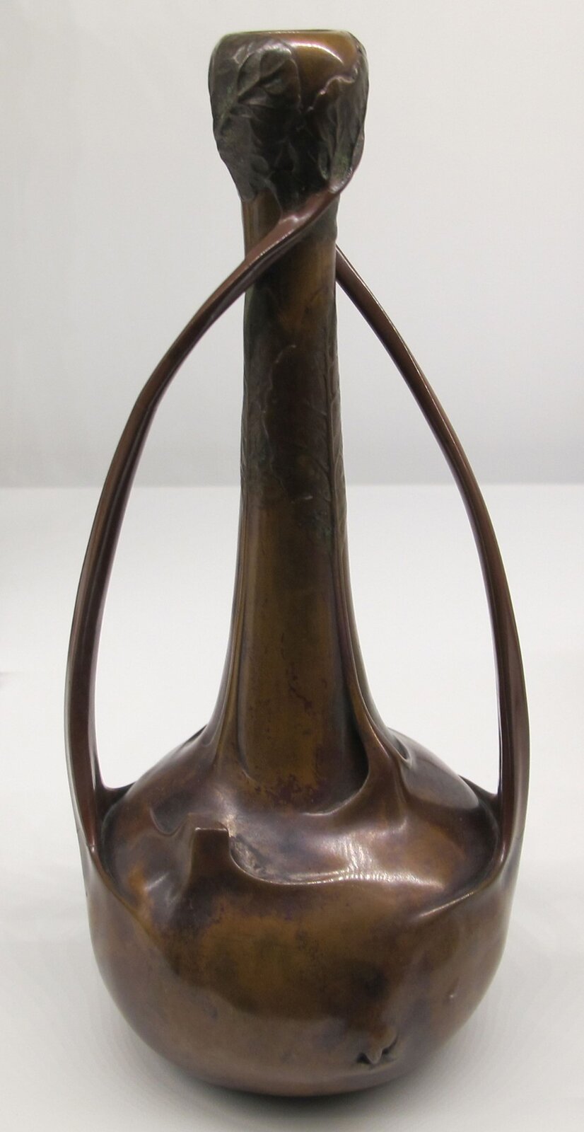 Ilustracja przedstawia „Wazon Chou” autorstwa Luciena Gaillarda. Wazon jest smukły i podłużny, wzdłuż wazonu pną się liście. Wazon jest w kolorze brązowym.