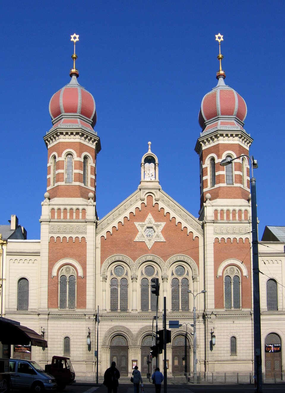 Zdjęcie przedstawia wielką synagogę w Pilźnie w Czechach. Budynek jest wysoki, centralna jego część posiada wieżyczkę, trzy półkoliste okna oraz półkoliste drzwi. Z dwóch stron budynku występują bliźniacze, ośmiokątne wieże. Nad wejściem do synagogi widoczna jest sześcioramienna gwiazda Dawida. Fasada budynku ma kolor kremowy i miejscami ceglastoczerwony. 