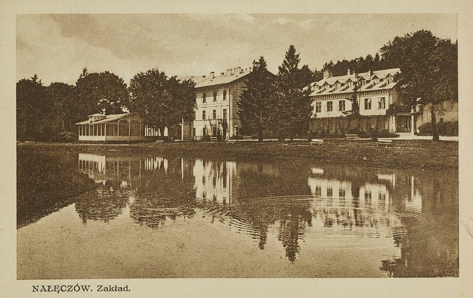 Pocztówka przedstawia rozległy staw, a za nim kilka zabudowań i dużą altanę. Są one otoczone drzewami.
