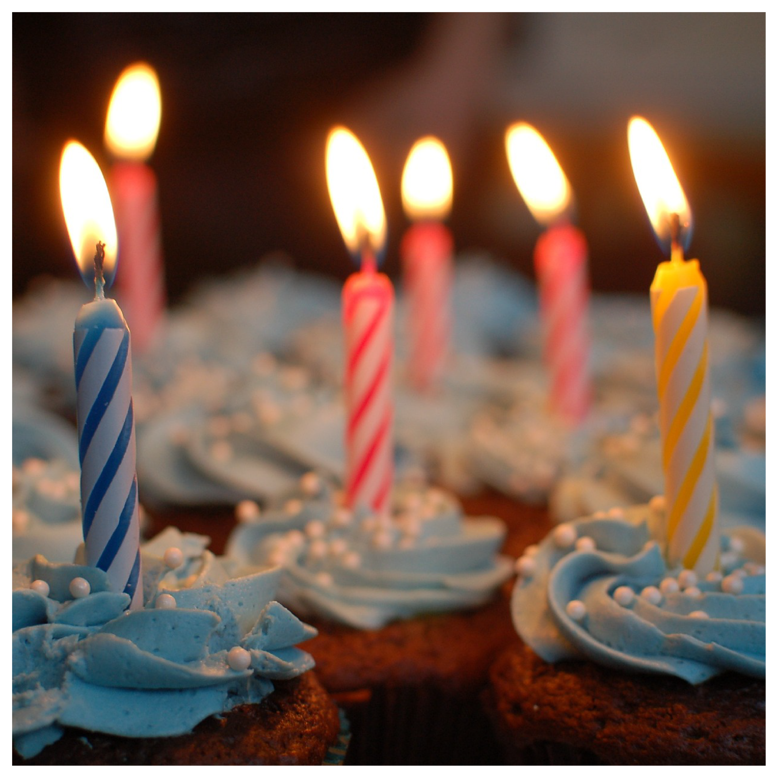 Zdjęcie przedstawia zapalone świeczki powkładane w babeczki z niebieskim kremem.