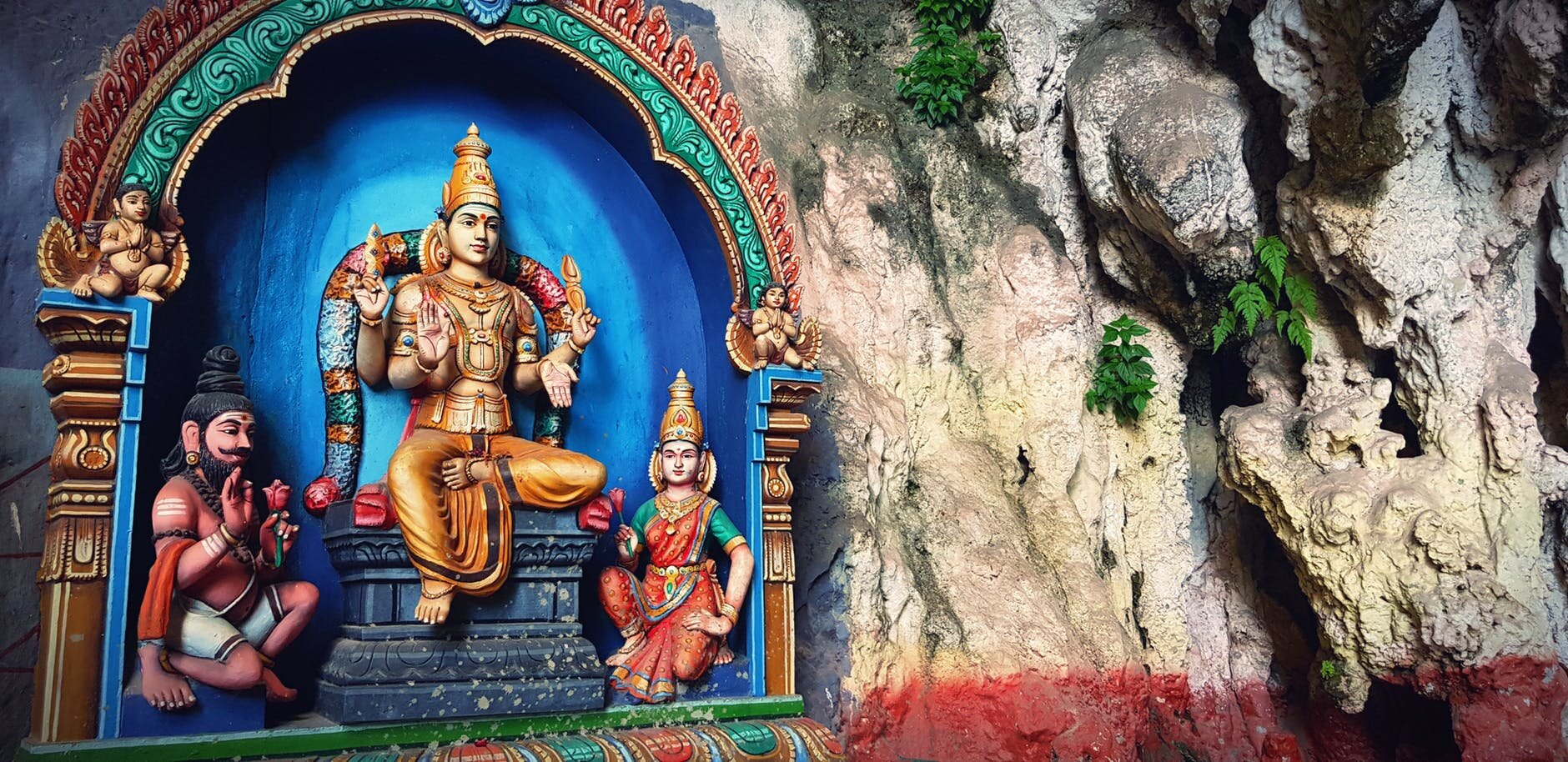 Zdjęcie przedstawia ołtarz z trzema postaciami. Jedna siedzi wyżej, dwie pozostałe niżej - to mężczyzna z kokiem na głowie i kobieta. Główne bóstwo ma cztery ramiona. 