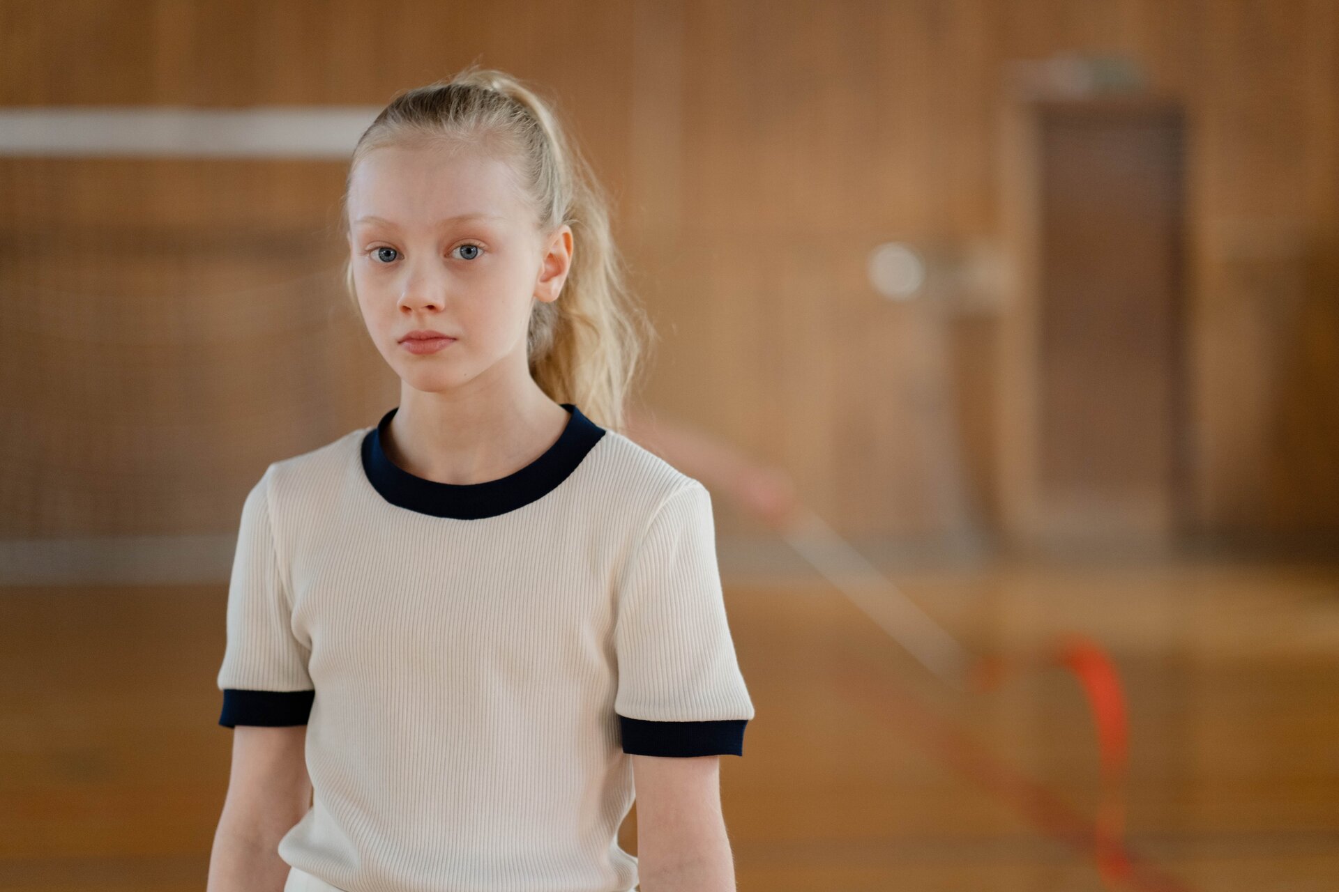 Zdjęcie przedstawia dziewczynkę ubraną w strój sportowy, która stoi w sali gimnastycznej.