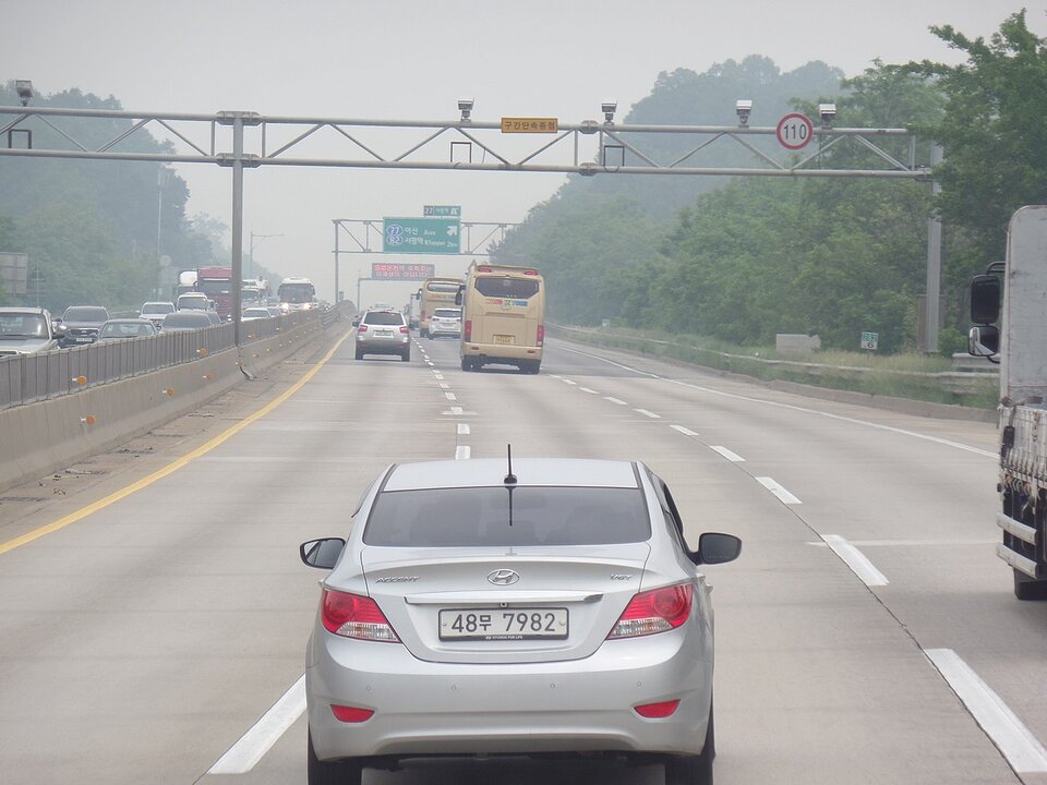 Zdjęcie przedstawia autostradę trzypasmową z poboczem, po której jadą samochody z widocznymi urządzeniami rejestrującymi prędkość.