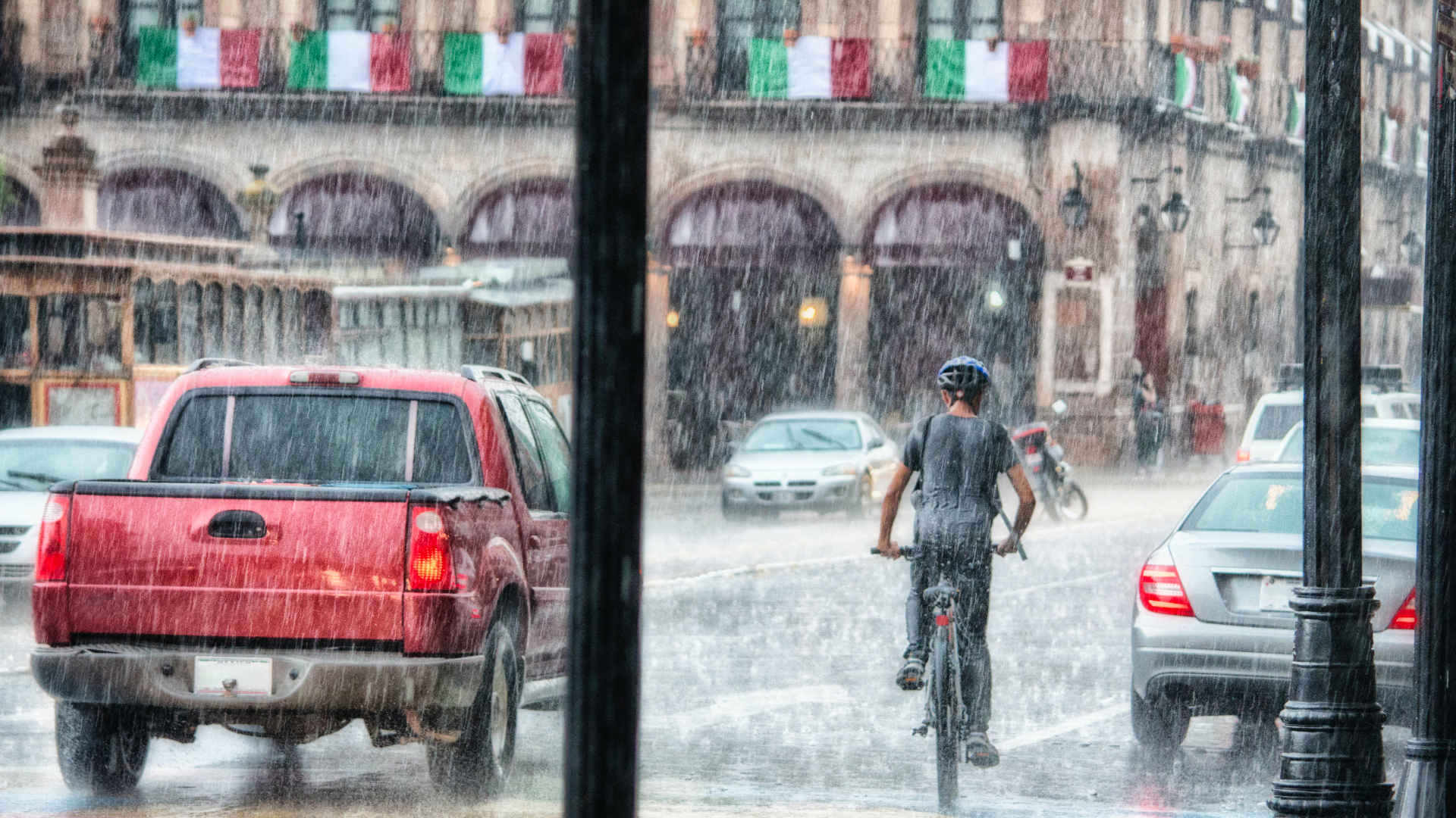 Zdjęcie przedstawia samochody i rowerzystę na ulicy w mieście w czasie deszczu.