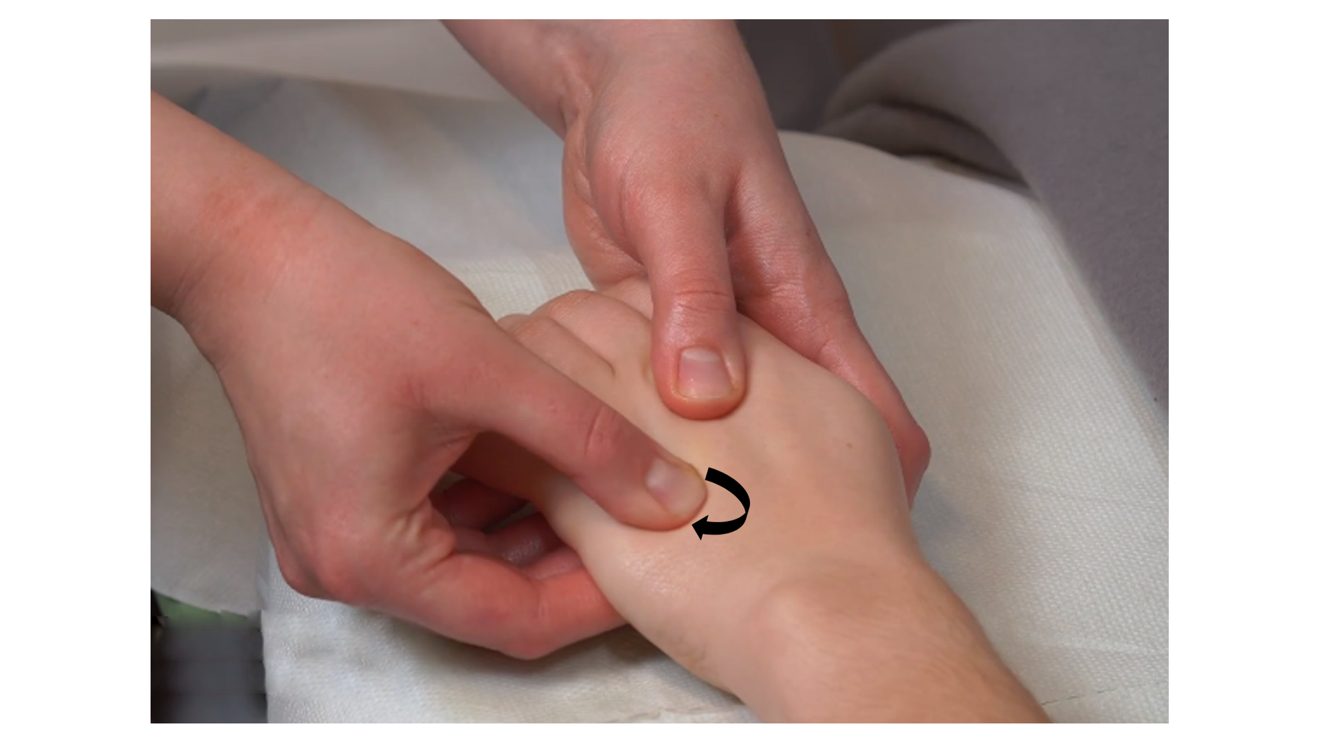 Zdjęcie pod tytułem rozcieranie powierzchowne i głębokie grzbietowej strony ręki. Zdjęcie przedstawia ręce masażysty obejmujące rękę pacjenta i wykonujące rozcieranie jej grzbietowej strony przy użyciu opuszków kciuków.