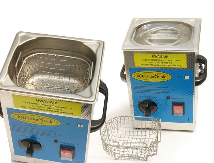 Zdjęcie przedstawia myjkę ultradźwiękową. To obudowany metalem, sześcienny zbiornik z dwoma uchwytami po bokach. Zbiornik ten ma na szczycie wgłębienie, w którym umieszczony jest metalowy kosz z dwoma rączkami skierowanymi ku górze. Zbiornik posiada metalową pokrywę z uchwytem. Na przedzie znajduje się regulator natężenia ultradźwięków, zabezpieczony plastikową pokrywą włącznik oraz kontrolna dioda wskazująca na temperaturę wyrażoną w stopniach Celsjusza. Na zbiorniku znajduje się napis: Uwaga!!! Przed uruchomieniem urządzenia zapoznać obsługę z dokumentacją techniczno‑ruchową.