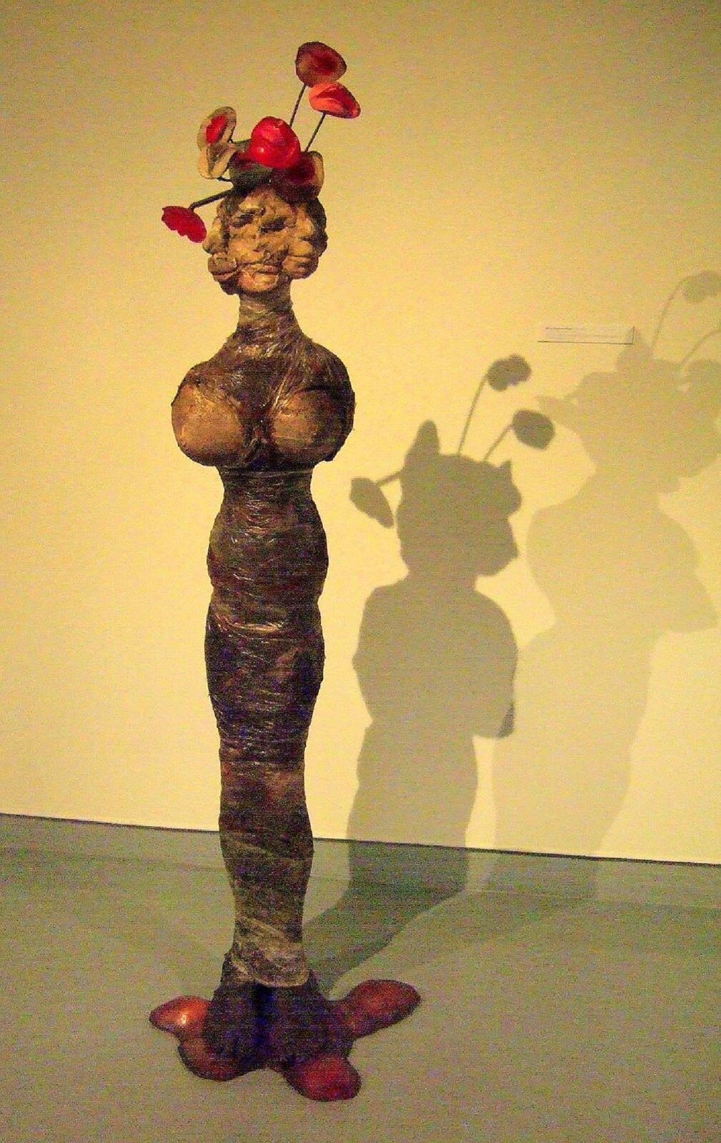 Zdjęcie przedstawia rzeźbę Aliny Szapocznikowej Bukiet II. Postać kobieca bez rąk, na głowie ma bukiet kwiatów, przypominających maki.