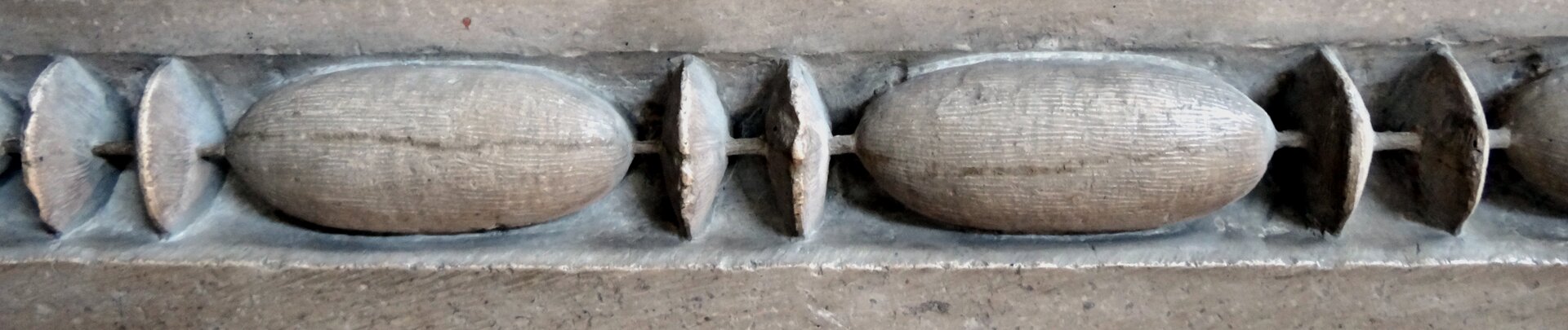 Fotografia przedstawia ornament, który składa się z rzędu kamiennych krążków i kołeczków. Elementy te ułożone są obok siebie - w tym przypadku: dwa krążki - kołeczek - dwa krążki. 