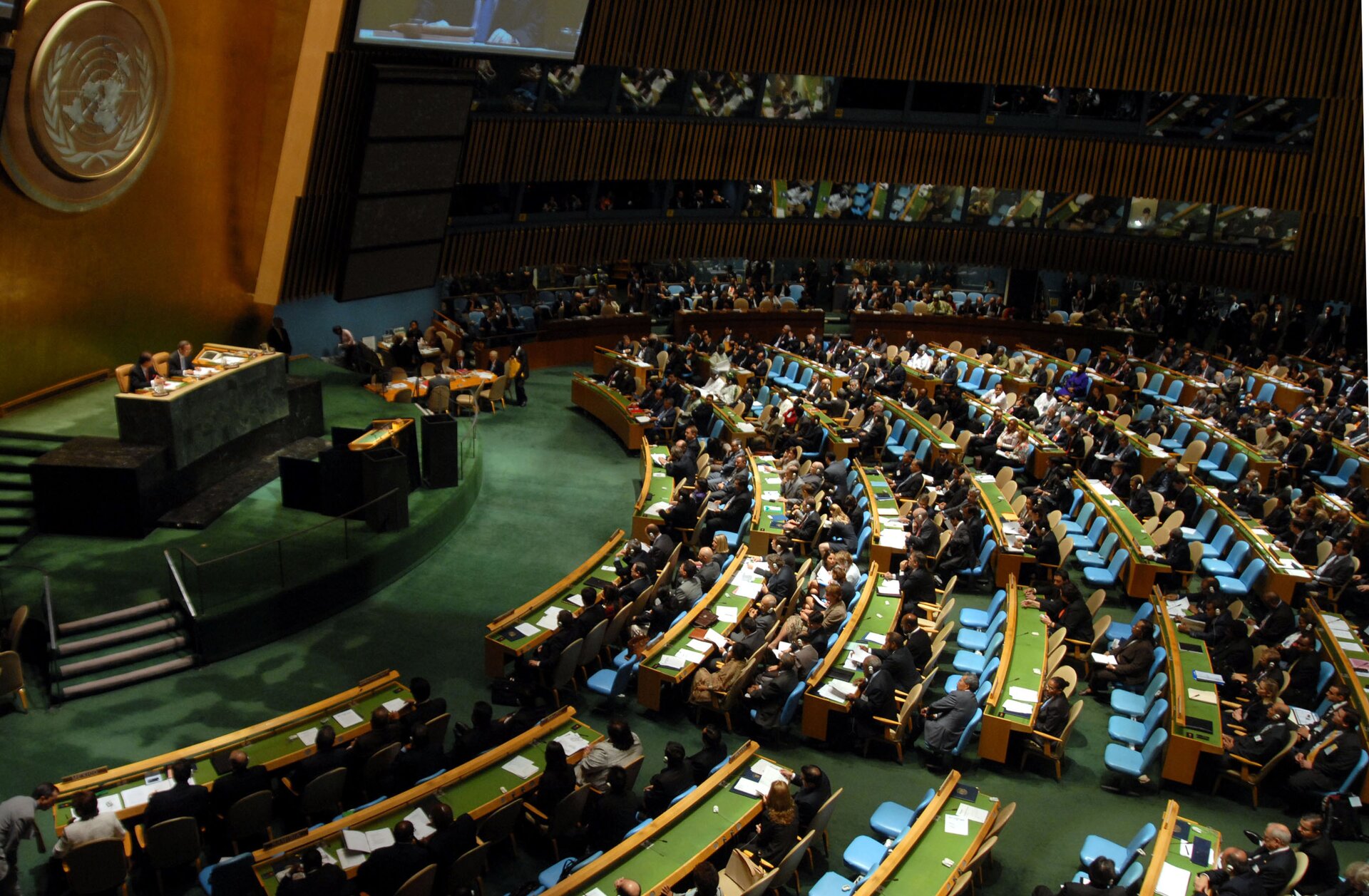Zdjęcie dużej sali. W części głównej widoczne logo ONZ (lewy górny róg zdjęcia). Na podwyższeniu za stołem zasiada Sekretarz Generalny ONZ. Poniżej znajduje się mównica. Do mównicy prowadzą schody (po lewej stronie zdjęcia). W pozostałej części sali umieszczone są krzesła dla przedstawicieli państw biorących udział w obradach, gości zaproszonych, mediów (prawa strona zdjęcia). Na stołach widoczne są kartki. Na górze zdjęcia zawieszony jest telebim.