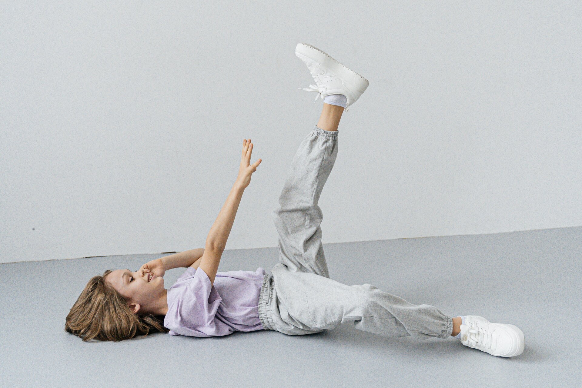 Ilustracja przedstawia ćwiczącą dziewczynkę. Leży ona na plecach i ma uniesioną nogę.