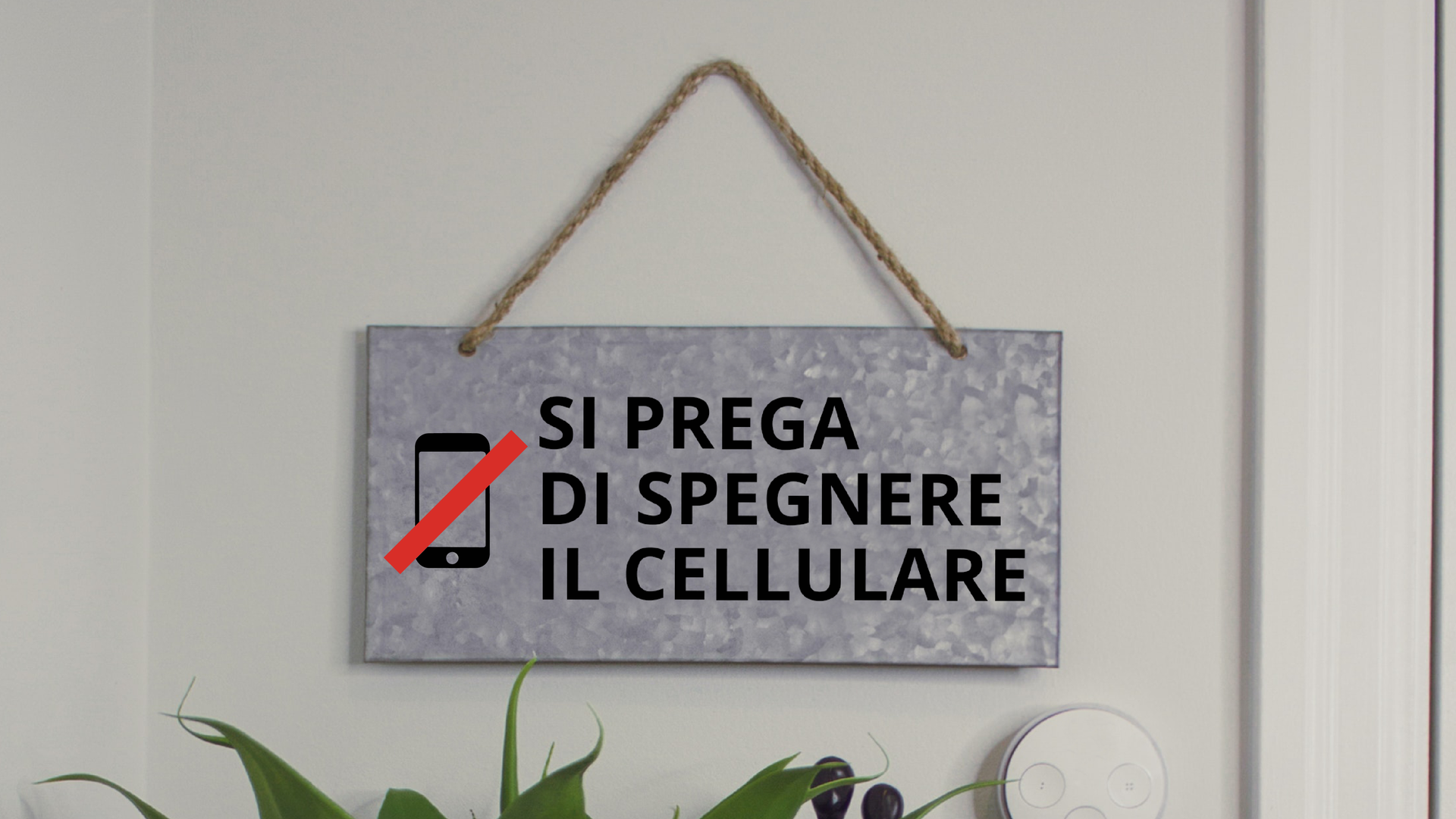 Zdjęcie przedstawia tabliczkę wiszącą na ścianie. Na tabliczce znajduje się ikona przekreślonego telefonu oraz napis: Si prega di spegnere il cellulare.