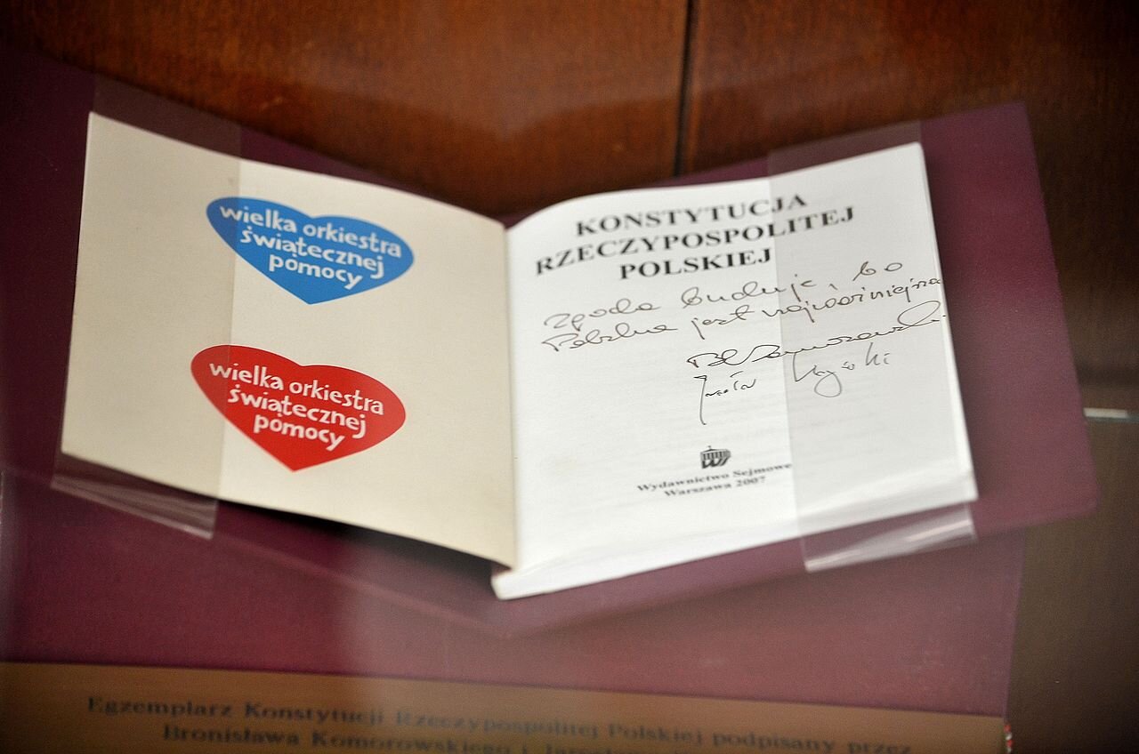 Zdjęcie przedstawia stronę tytułową Konstytucji. Widnieją na nim podpisy Bronisława Komorowskiego i Jarosława Kaczyńskiego, a także dwa serduszka z napisem Wielka Orkiestra Świątecznej Pomocy.
