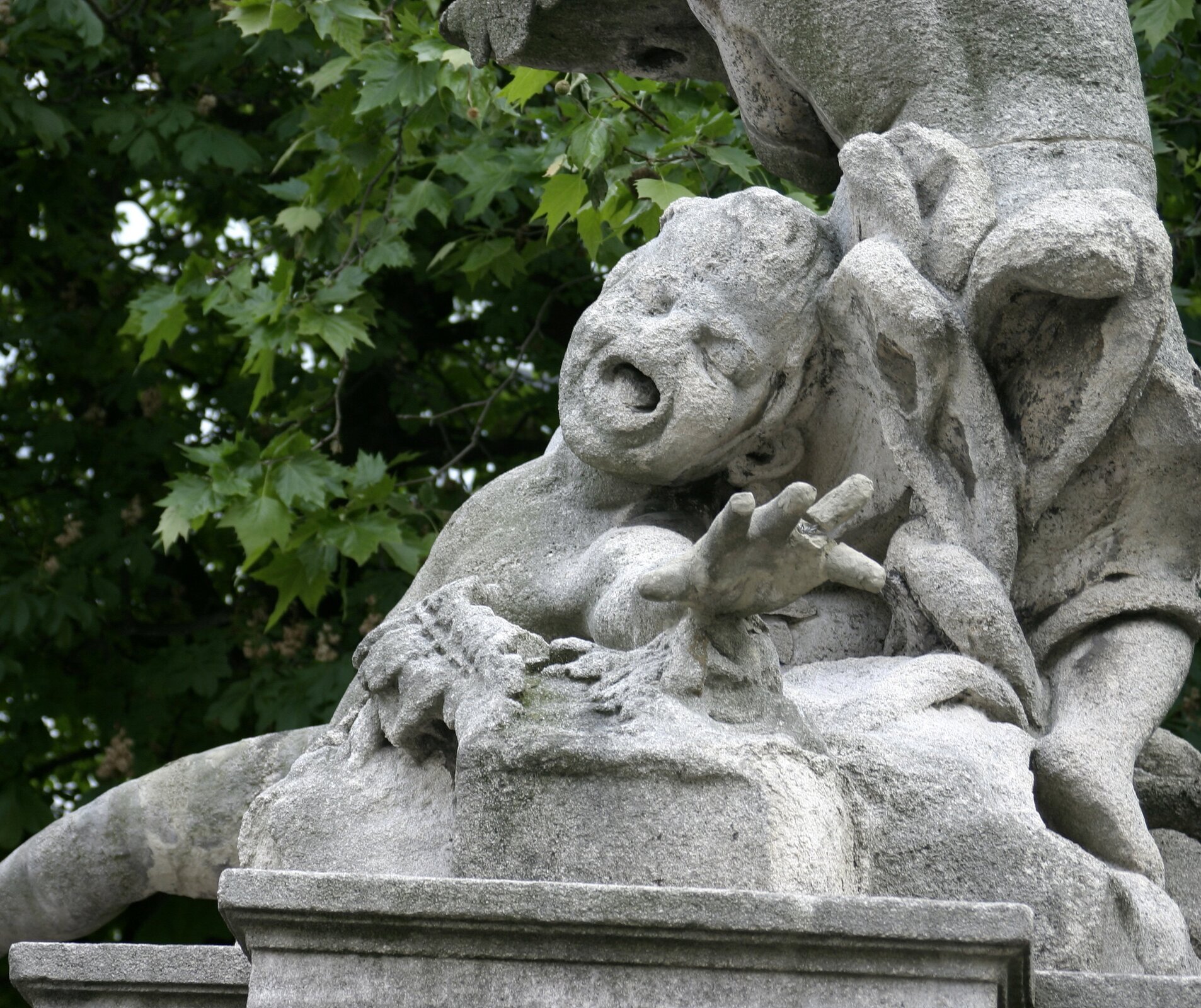 Zdjęcie przedstawia fragment jasnej rzeźby dziecka wyciągającego przed siebie dłoń w geście rozpaczy. Rzeźba wykonana jest z jasnego materiału. Rzeźba jest zniszczona, na przykład na twarzy dziecka brakuje nosa.  