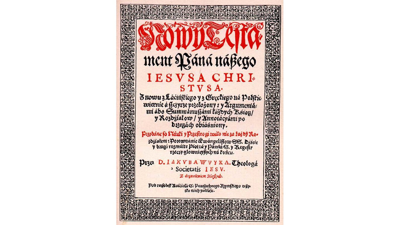 Fotografia przedstawia stronę z jednego z wydań Biblii. Litery przywodzą na myśl gotyk, są czarne i czerwone, trudne do odczytania przez to, jak zdobne. Wokół tekstu umieszczono ozdobną ramkę, która składa się z misternego wzoru. The photograph shows a page from one of the editions of the Bible. The letters resemble Gothic, they are black and red, difficult to read by how remarkable. Around the text there is a decorative frame, which consists of an intricate pattern.