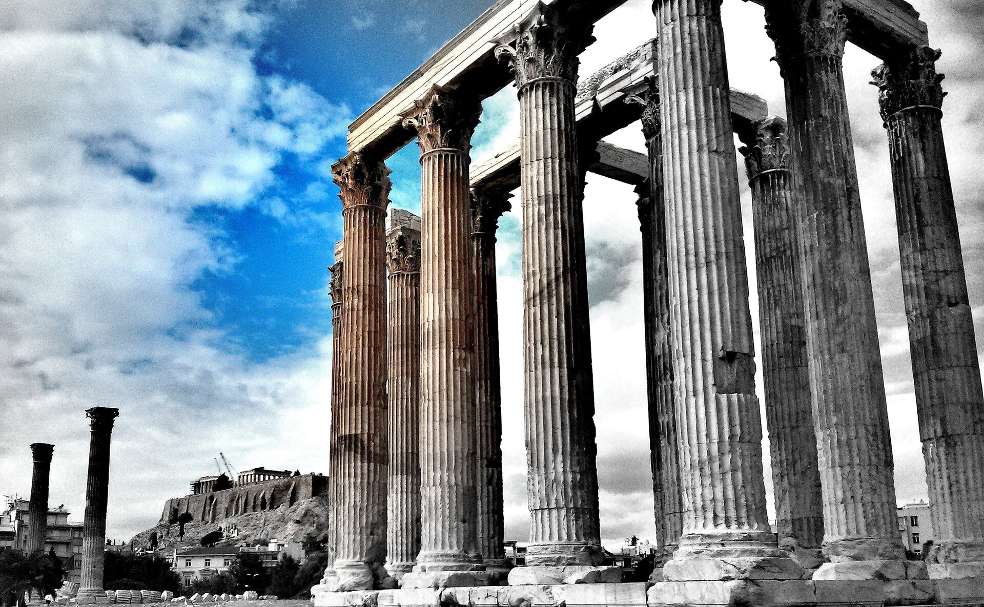 Zdjęcie przedstawia ruiny świątyni Zeusa Olimpijskiego w Atenach. Widoczne są nieliczne, zachowane kolumny korynckie zwieńczone liśćmi akantu. 