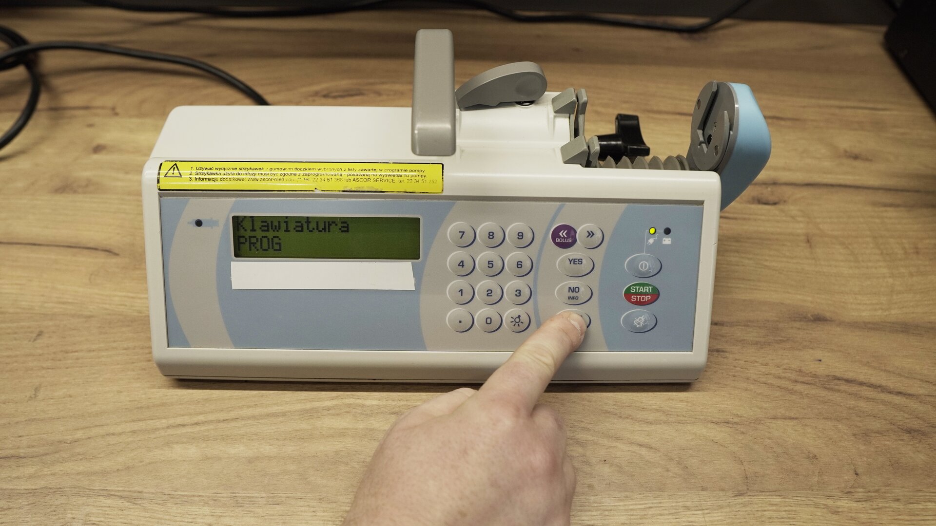 Na zdjęciu technik przeprowadza test klawiatury pompy infuzyjnej. Na ekranie wyświetlana jest informacja: "Klawiatura PROG.". Technik wciska przycisk PROG SETUP na aparacie.