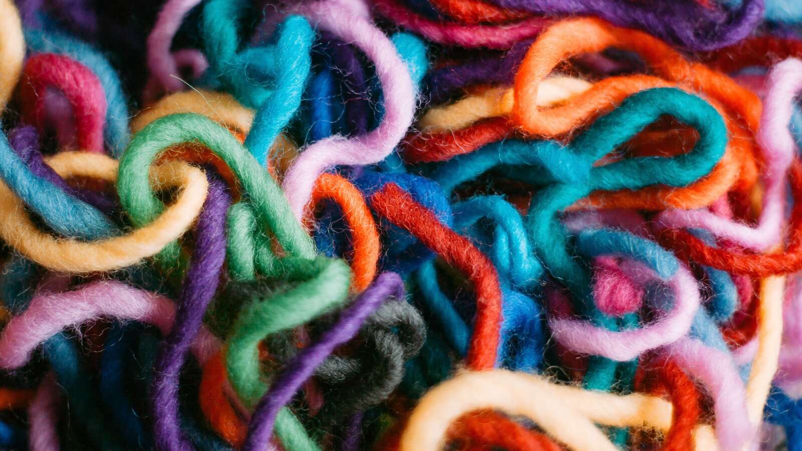 Zdjęcie przedstawia zbliżenie na różnokolorowe, poplątane włóczki.