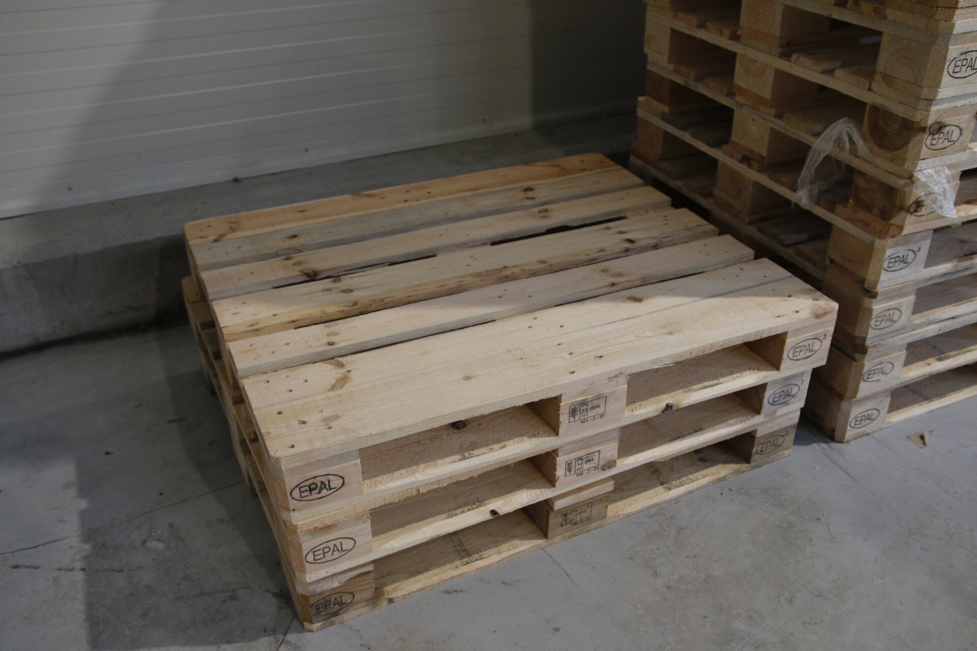 Zdjęcie przedstawia ułożone na sobie drewniane palety. Palety mają oznaczenie E P A L. 