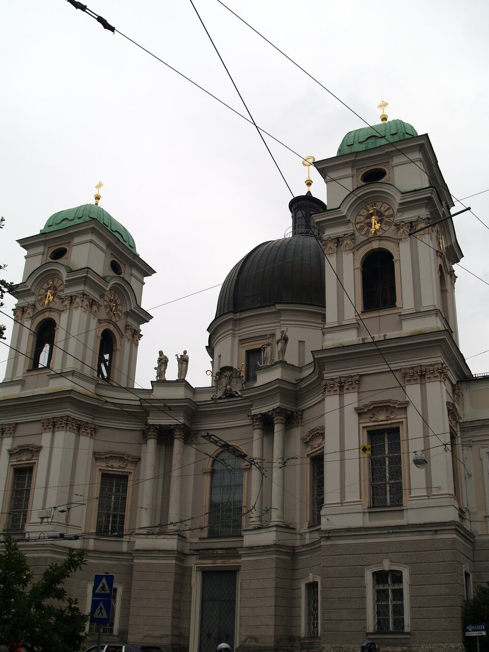 Ilustracja przedstawia zdjęcie budynku zaprojektowanego przez Johanna Bernharda Fischer von Erlacha, kościół Świętej Trójcy w Salzburgu. Wklęsła fasada świątyni, ujęta dwiema wieżami na planie prostokąta, połączona jest z dwoma skrzydłami seminarium. Proste, pozbawione dekoracyjnego portalu wejście flankują wysunięte przed lico muru dwie pary monumentalnych kolumn na wysokich cokołach. Na szczycie odcinków belkowania ustawione są cztery figury, personifikacje boskiej mądrości oraz trzech cnót teologalnych: wiary, nadziei i miłości. Dolna kondygnacja fasady ozdobiona jest boniowaniem pasowym. Korpus nawowy wieńczy kopuła osadzona na bębnie.