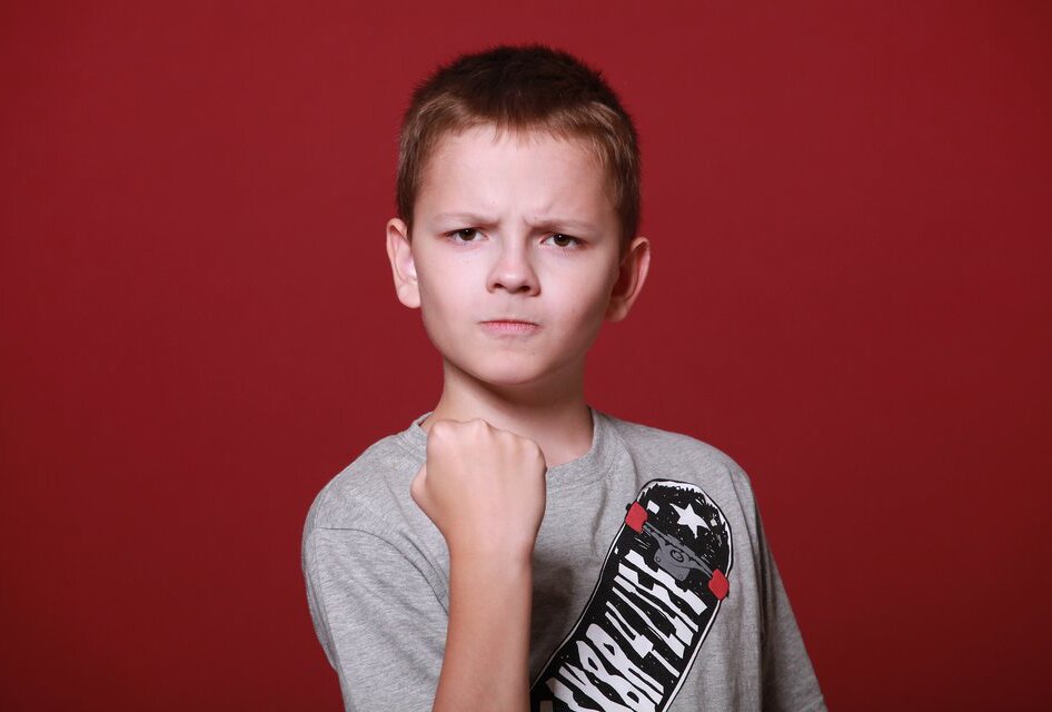Fotografia kolorowa przedstawia chłopca z poważną, zezłoszczoną miną. Przed sobą trzyma zaciśniętą pięść.