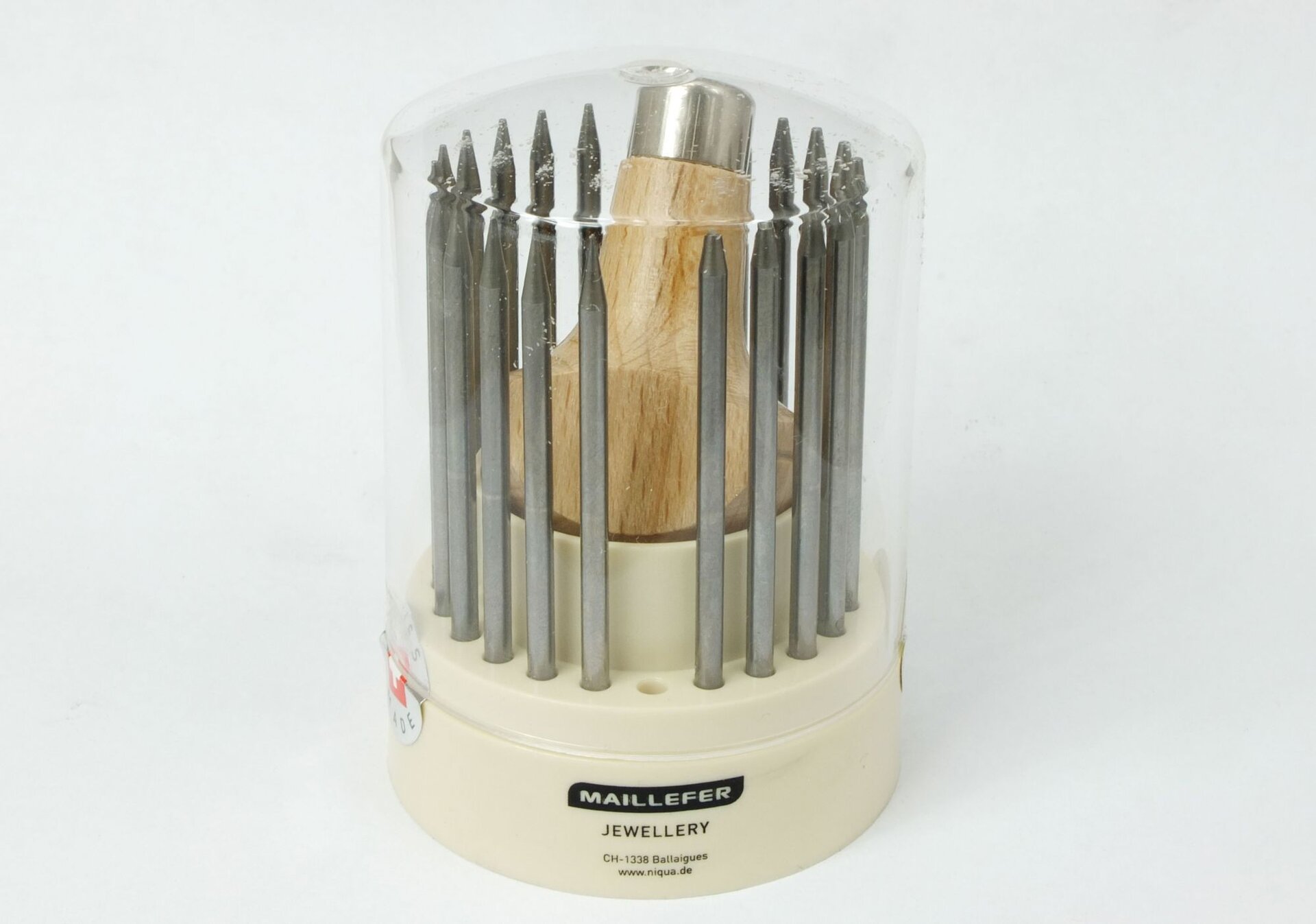 Zdjęcie przedstawia zestaw kilkunastu kornaisenów służących do oprawiania kamieni. Zestaw znajduje się w okrągłym pudełku z otworami. Jest wykonane z tworzywa sztucznego. W środku znajduje się drewniany uchwyt w kształcie grzybka, z mosiężną tuleją w środku. Kornaisteny są metalowe, długie i walcowate, ze spiczastymi zakończeniami w różnych rozmiarach.