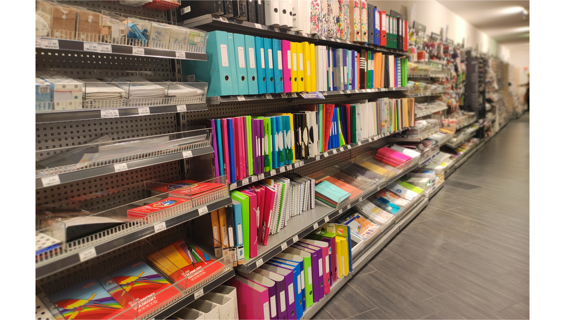 Zdjęcie przedstawia regał z artykułami papierniczymi w sklepie.